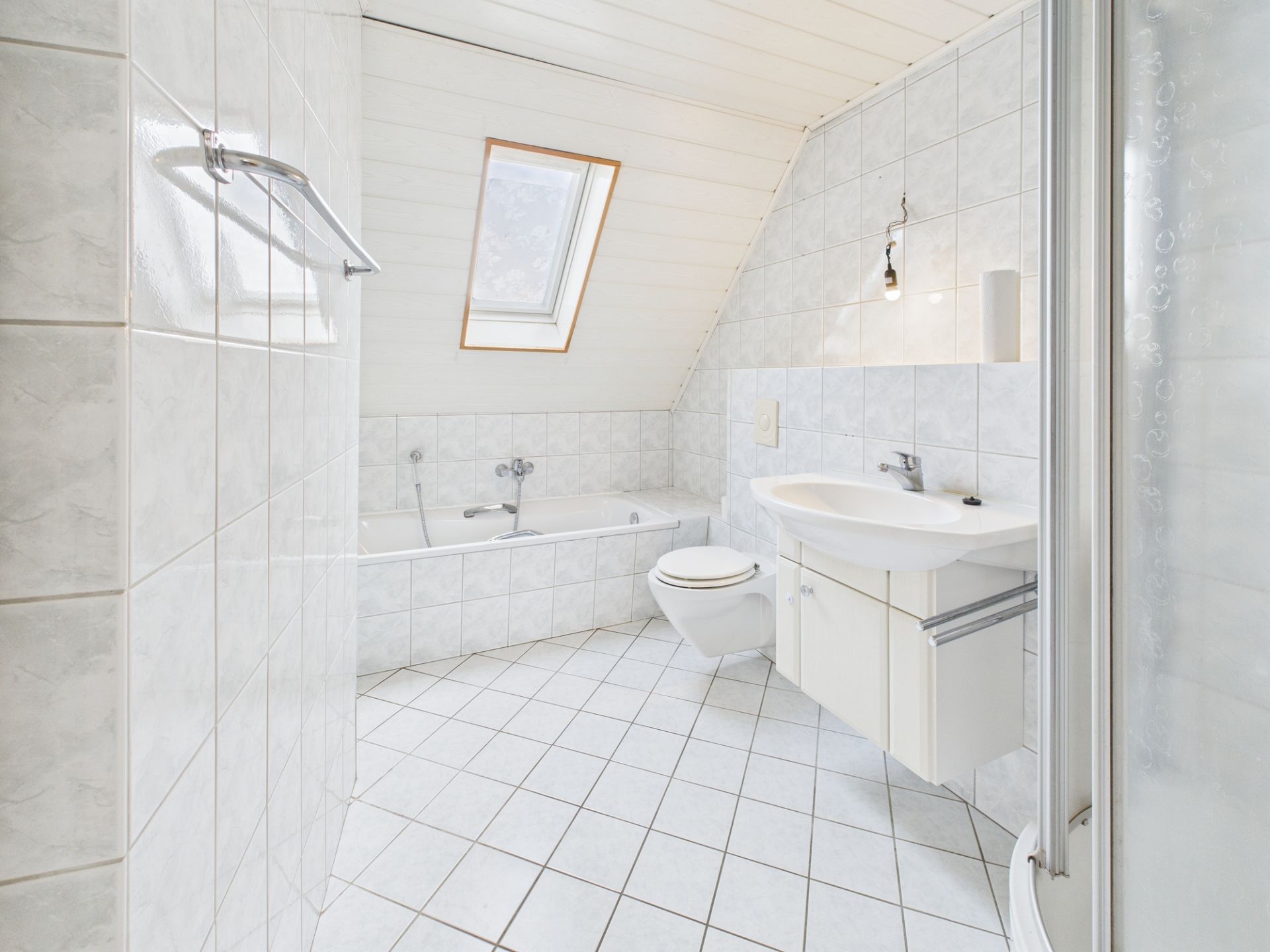 Helles Badezimmer mit Badewanne, Waschbecken, Toilette und Dachfenster.