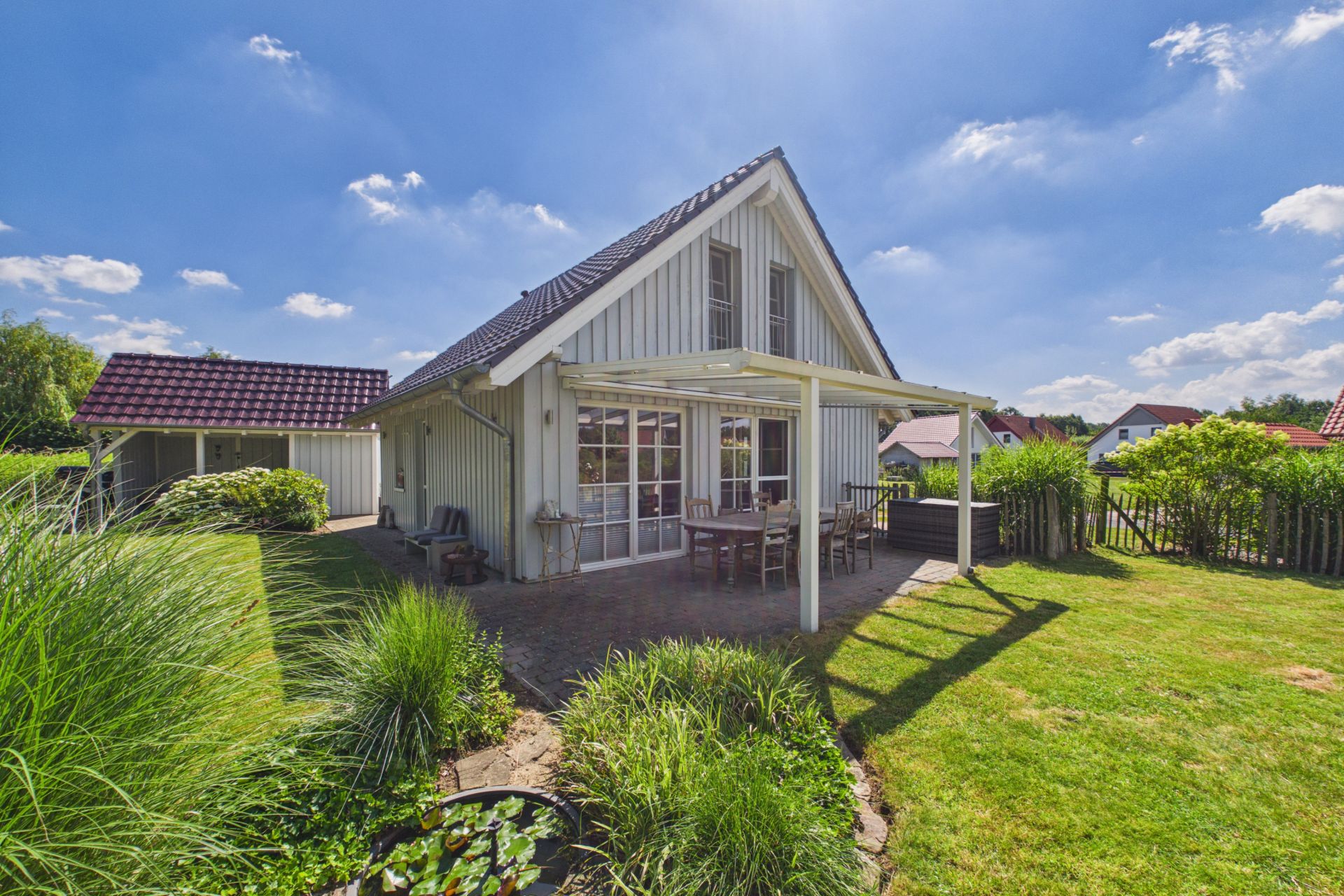 Einfamilienhaus mit Terrasse und Garten unter blauem Himmel.