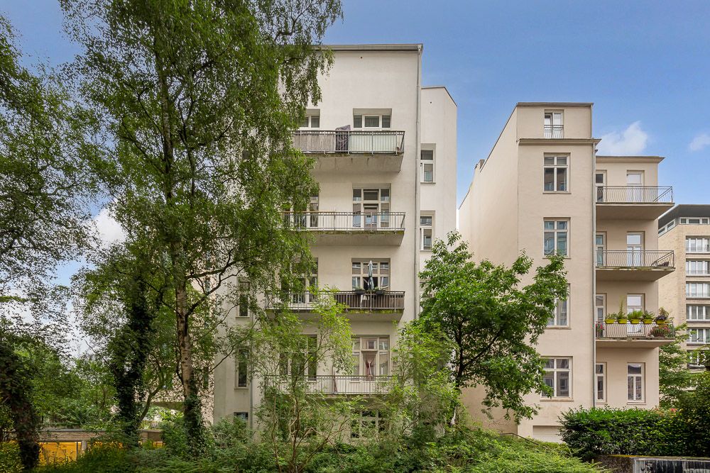 Mehrstöckiges Wohngebäude mit Balkonen, umgeben von Bäumen und Grünflächen.