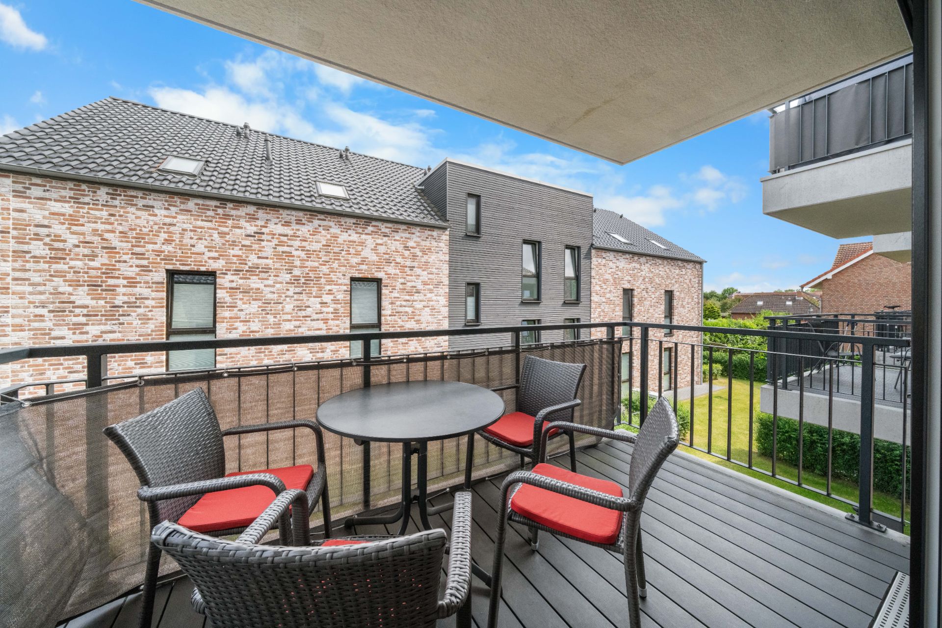 Balkon mit rundem Tisch und vier Stühlen mit roten Kissen, Blick auf Nachbarhäuser.