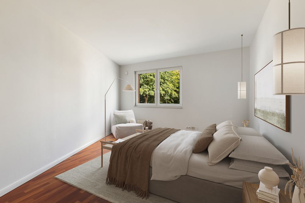 Helles Schlafzimmer mit Doppelbett, Sessel, Stehlampe und Fenstern mit Blick auf Bäume.