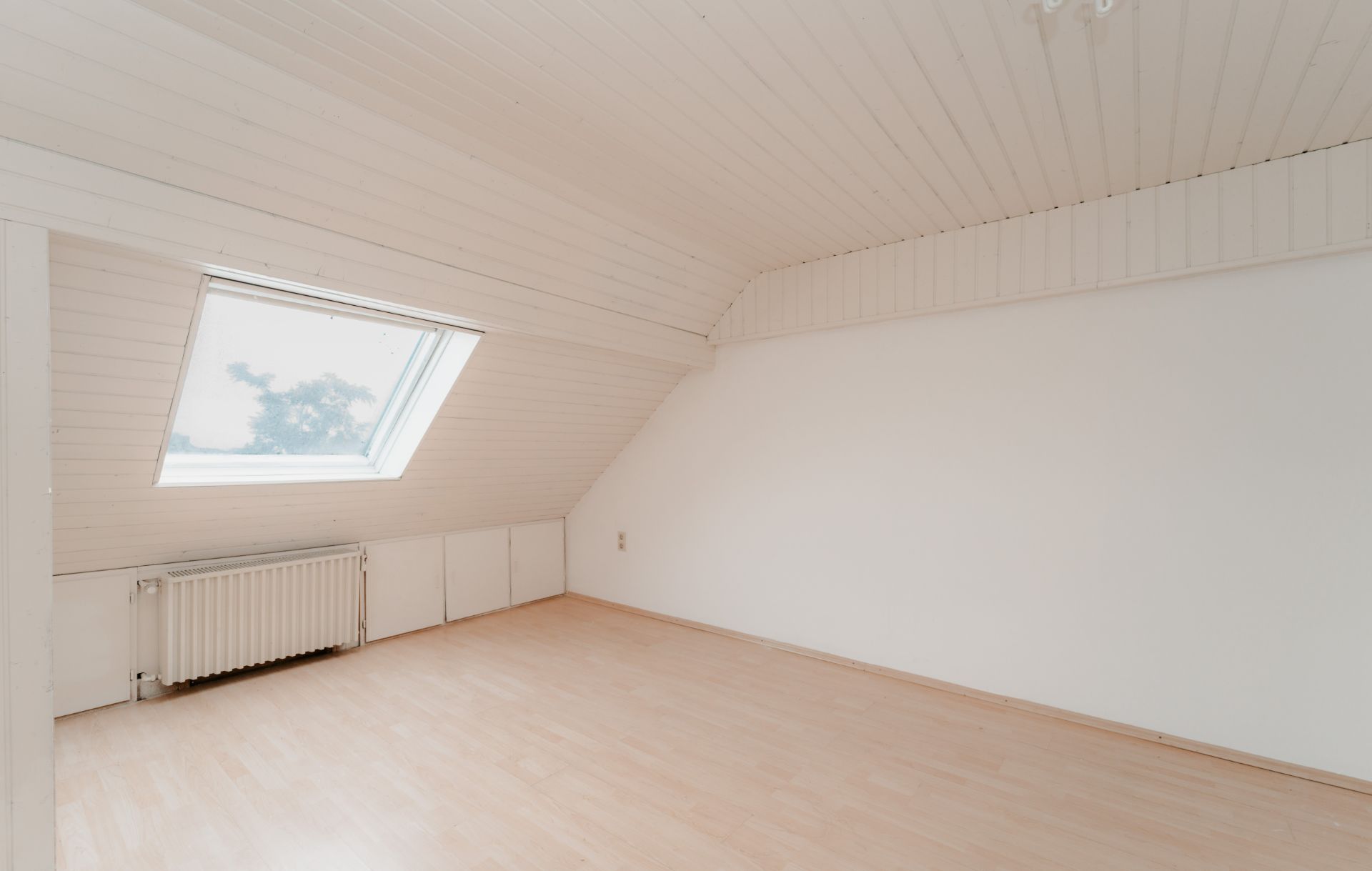 Helles Dachgeschosszimmer mit Schrägdecke, großem Fenster und Heizkörper.