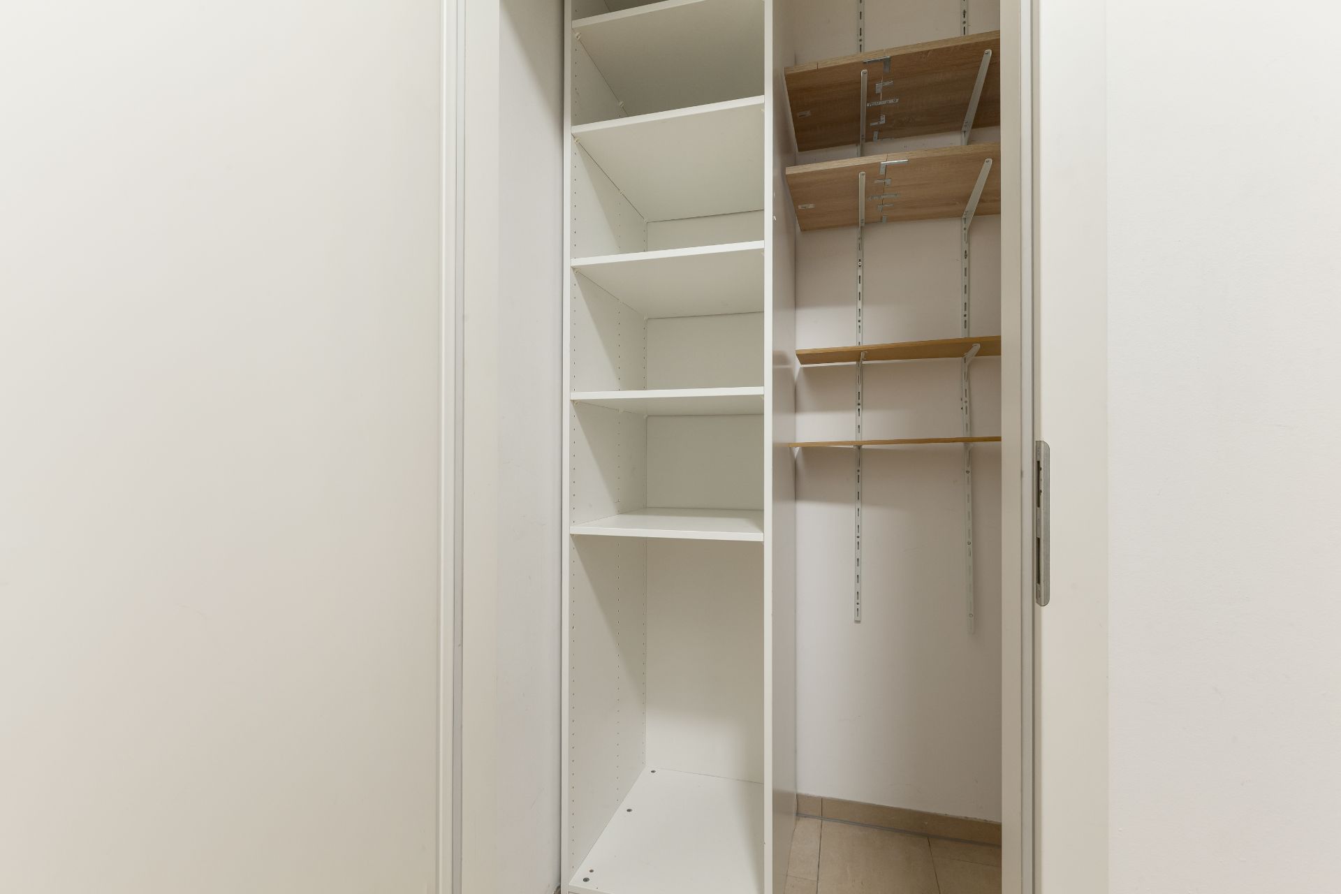 Offener Einbauschrank mit weißen und holzfarbenen Regalböden in einem hellen Raum.
