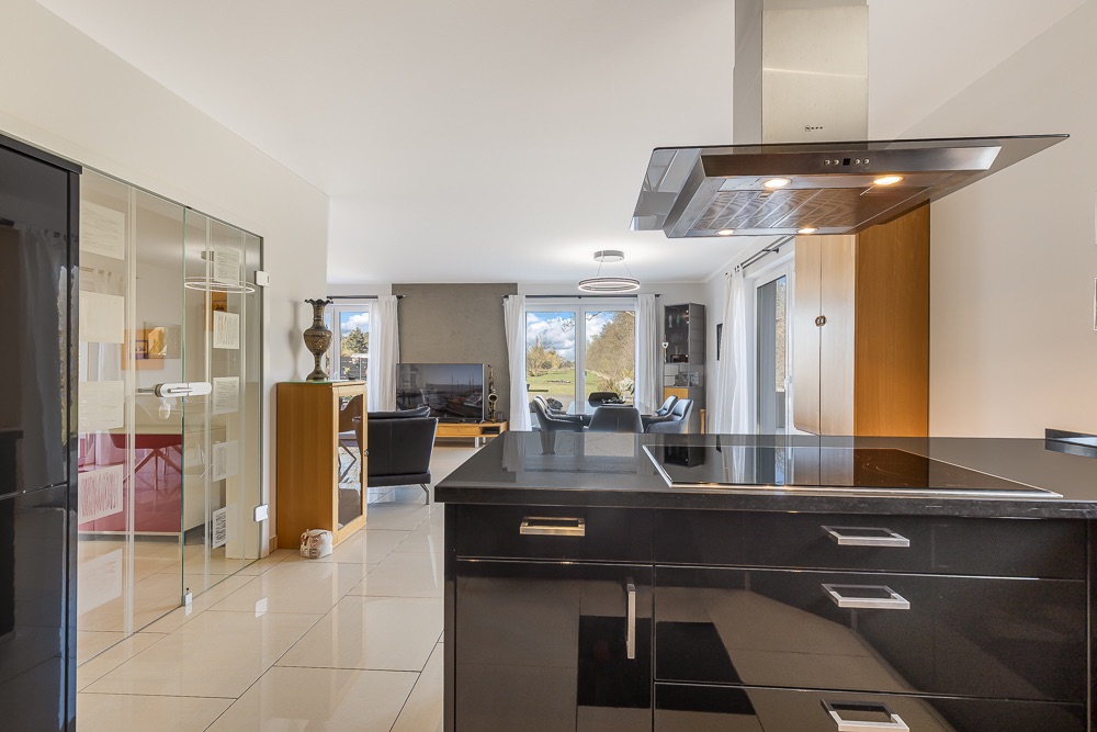 Moderne Küche mit Kochinsel und Blick ins helle Wohnzimmer mit großen Fenstern.