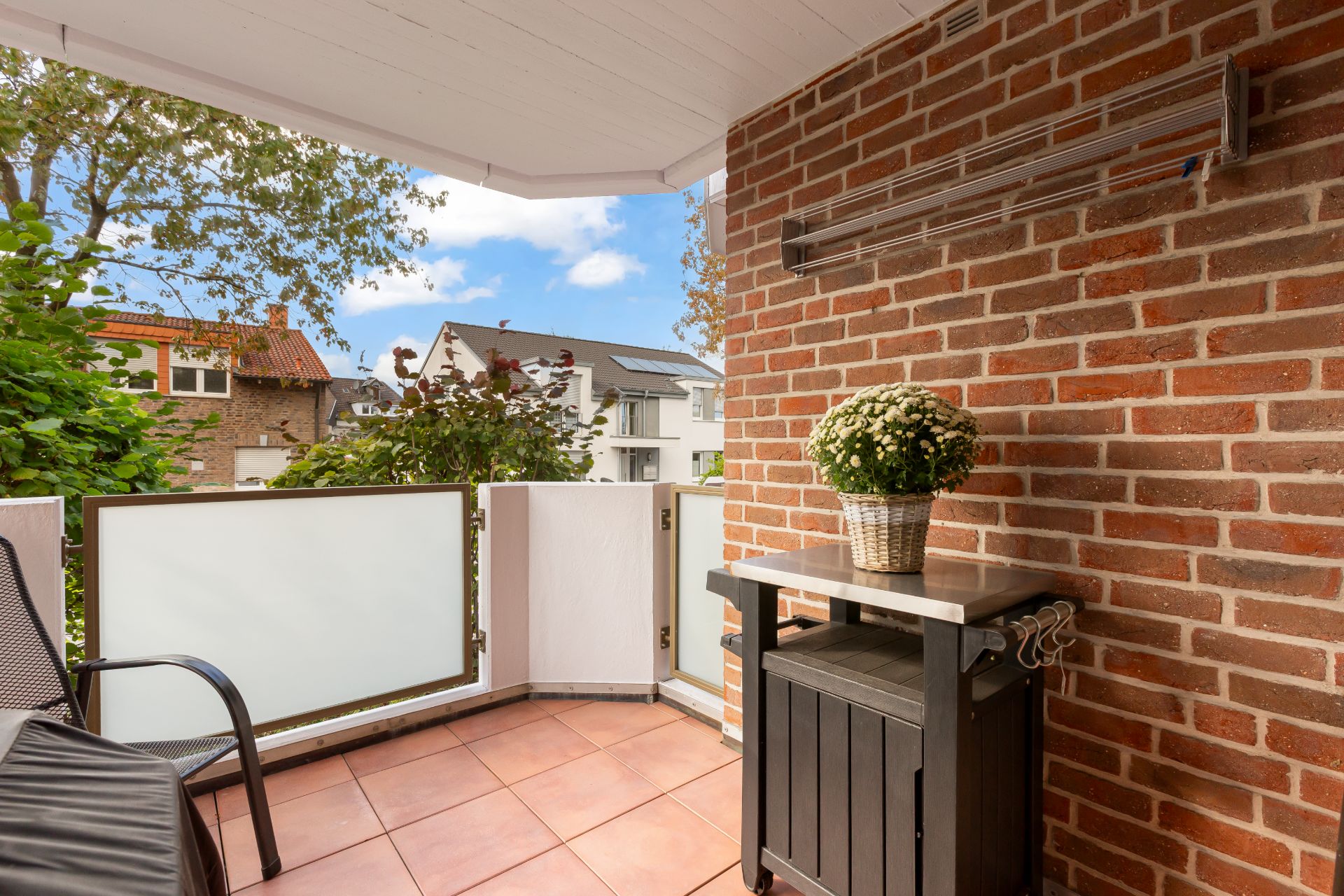 Balkon mit gemauerter Wand, Tisch, Stuhl und Blume im Korb, Blick auf Nachbarhäuser.