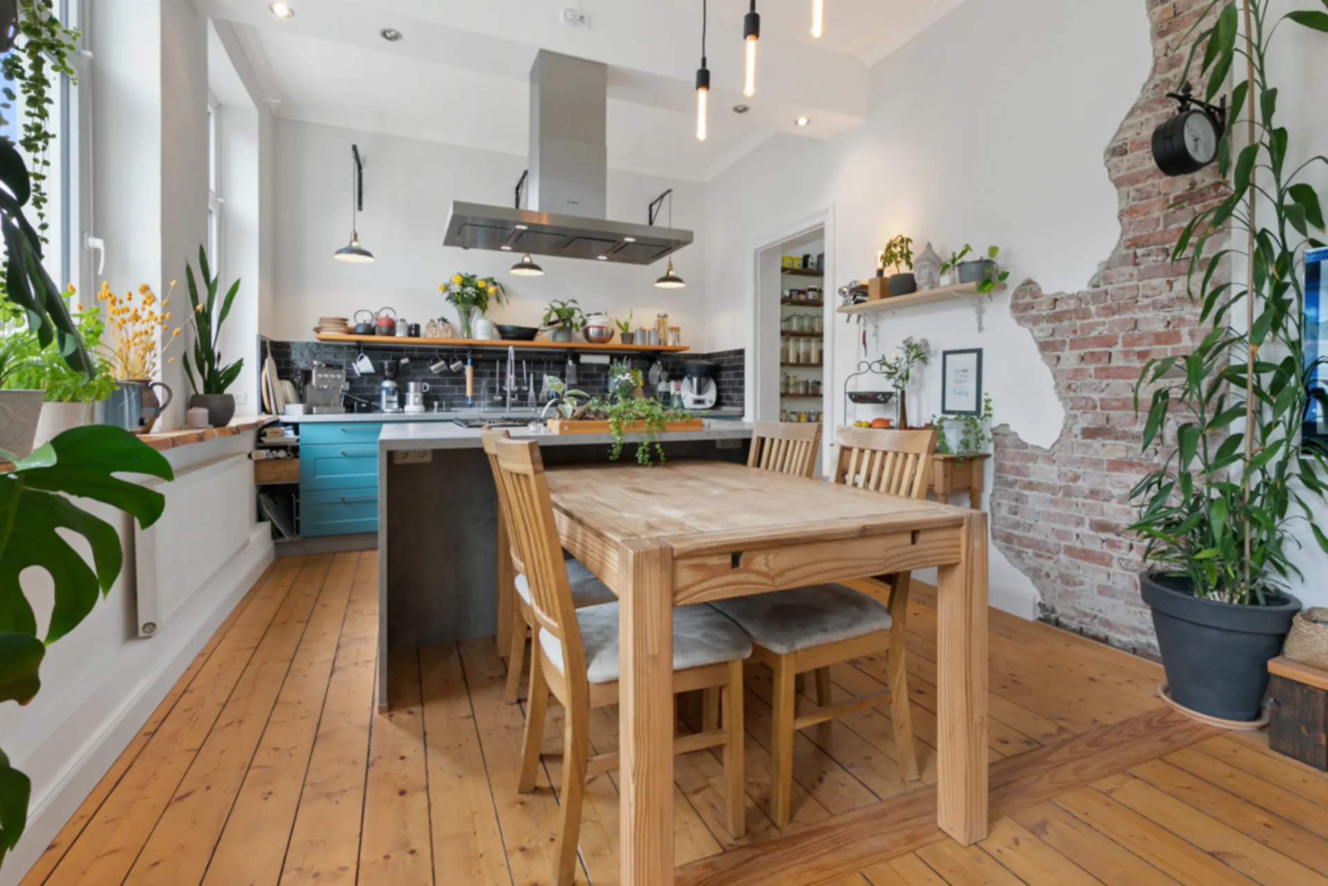 Helle Küche mit Holzboden, Esstisch, vielen Pflanzen und gemauerter Wand.