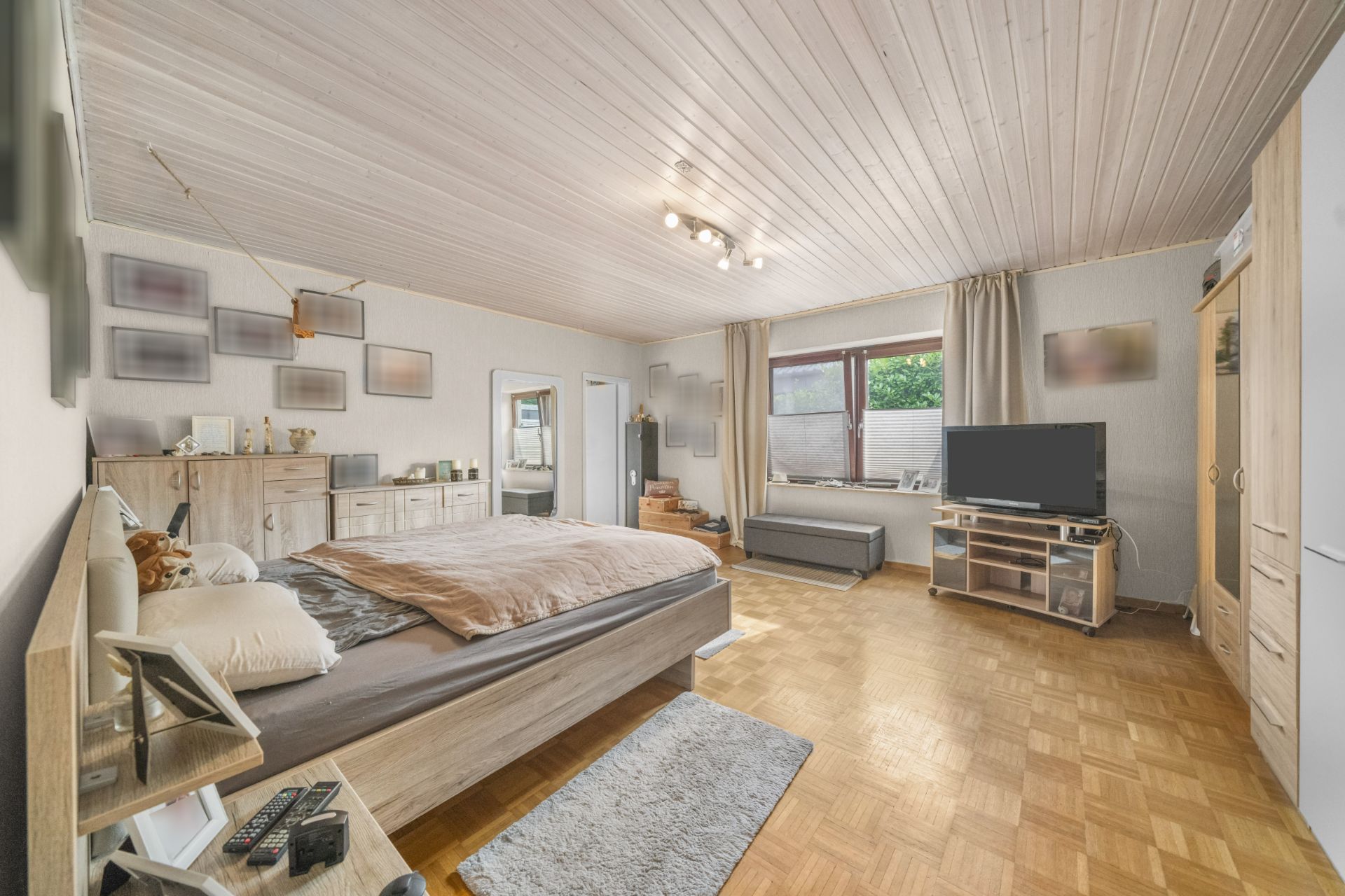 Geräumiges Schlafzimmer mit Doppelbett, Kommode, Fernseher und großem Fenster.