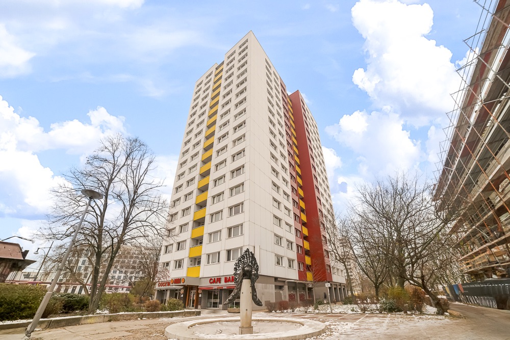 Hohes Wohngebäude mit gelben Balkonen und umliegenden Bäumen bei Tag.