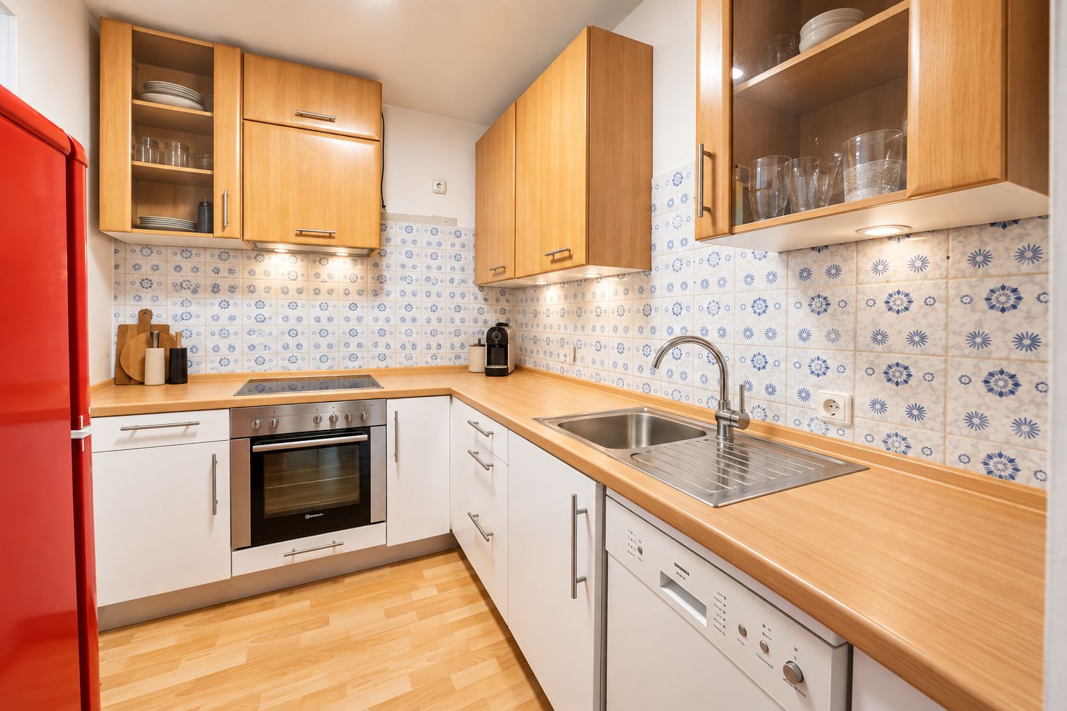 Moderne Küche mit Holzschränken, blauer Fliesenwand, Herd, Spüle und rotem Kühlschrank.