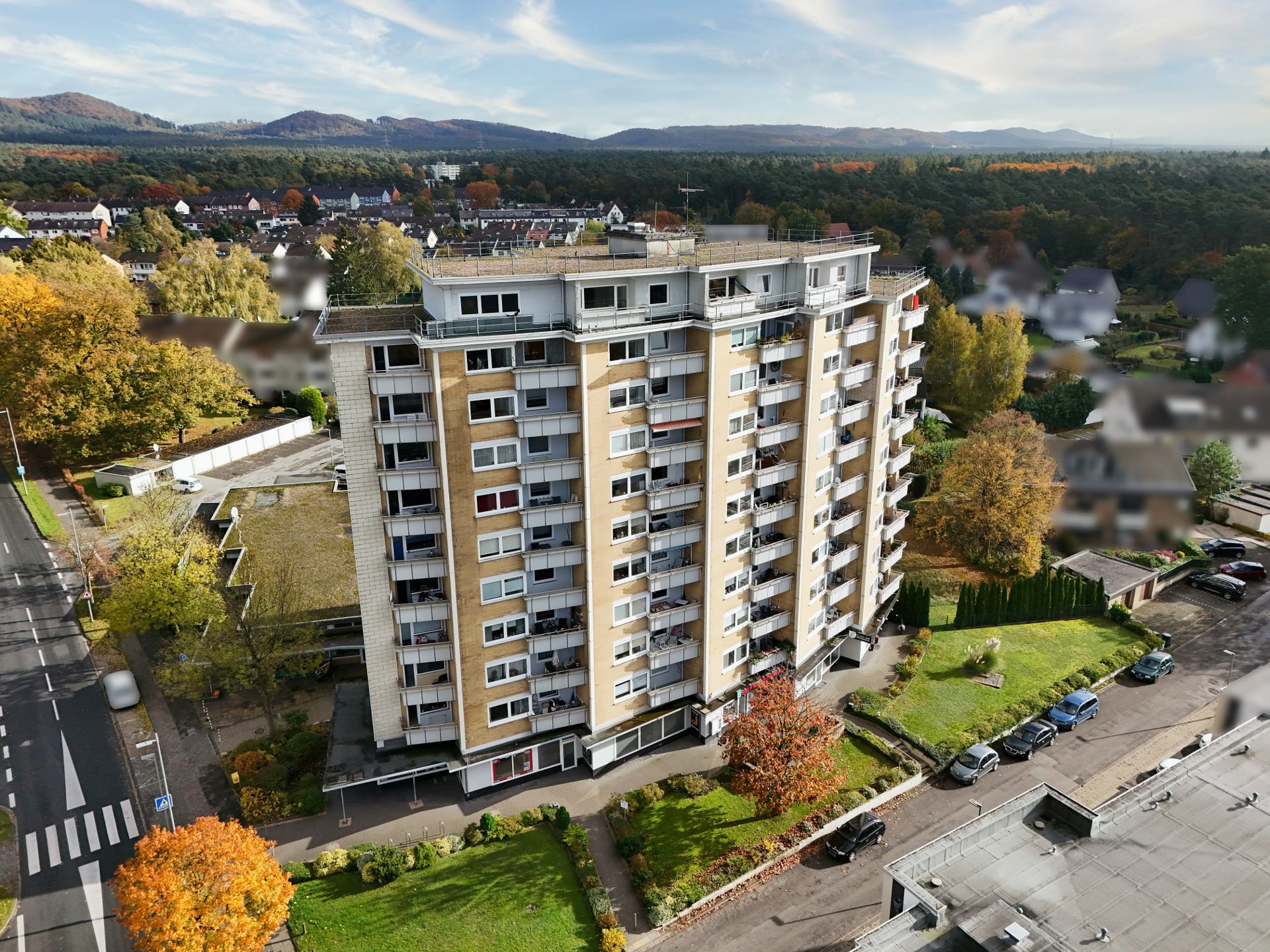 Mehrstöckiges Wohnhaus mit Balkonen, umgeben von Bäumen und Straßen, aus der Vogelperspektive.