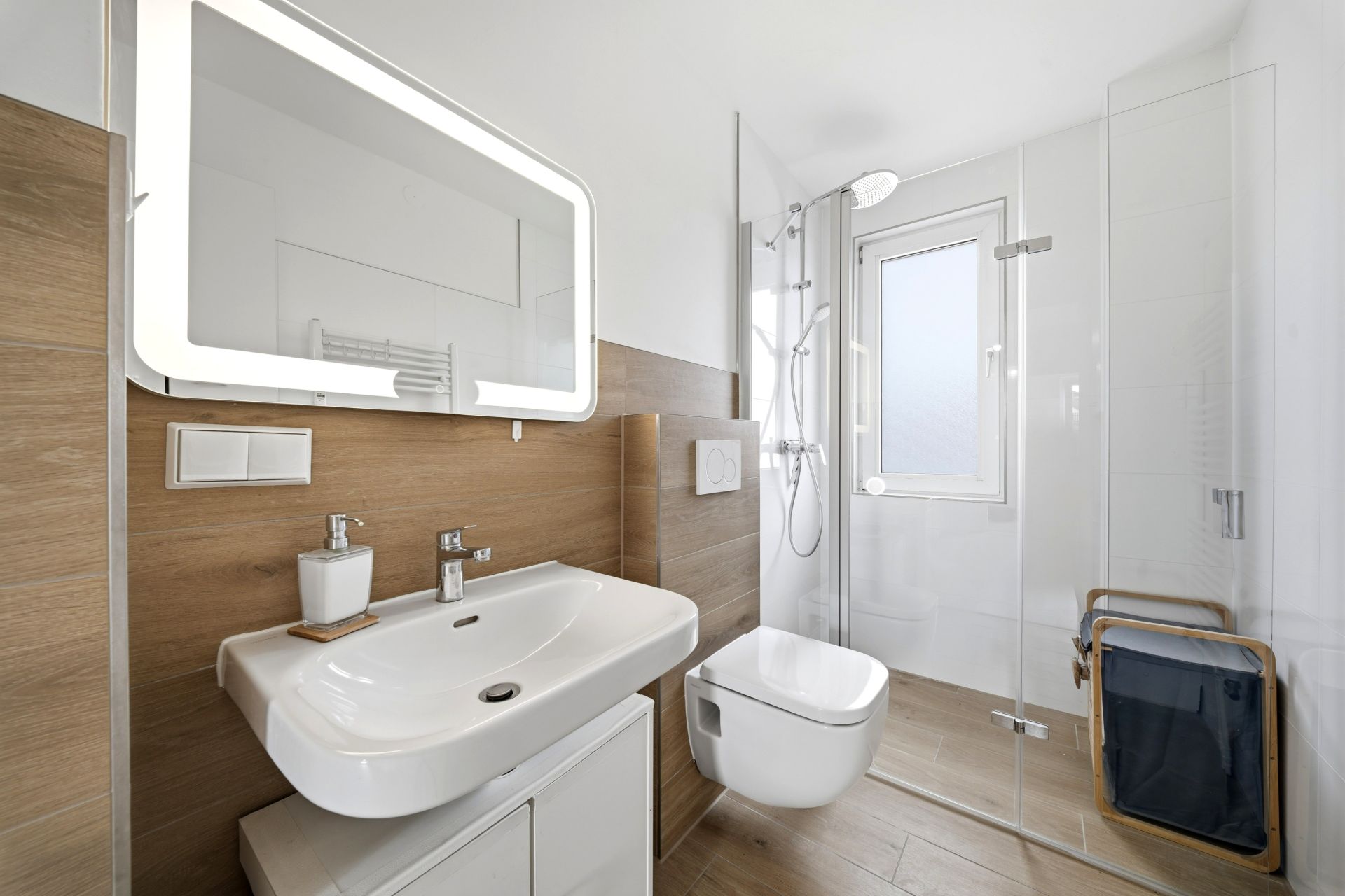Modernes Badezimmer mit Waschbecken, Spiegel, Wandtoilette und Dusche mit Glaswand.