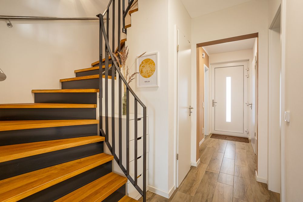 Heller Flur mit Holztreppe, weißen Wänden und einer weißen Haustür.