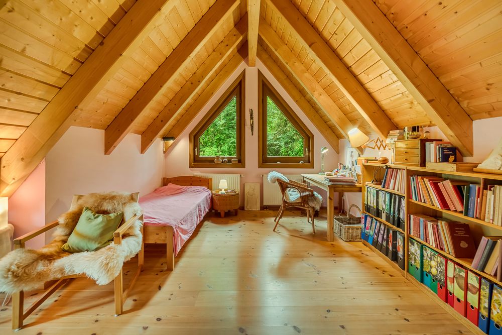 Gemütliches Dachzimmer mit Holzdecke, Bett, Schreibtisch und Bücherregal.