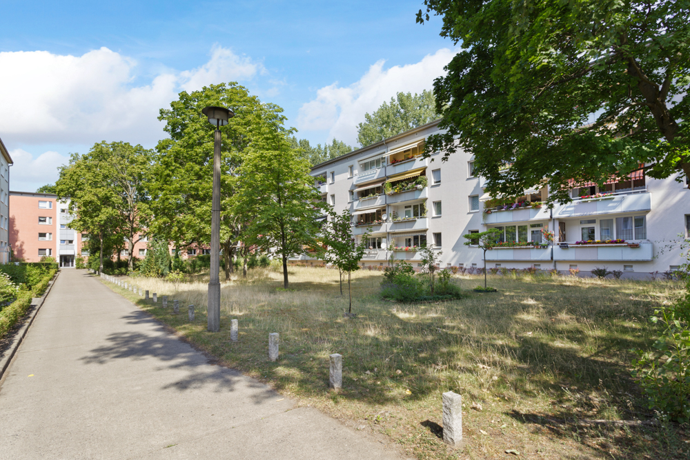 Wohngebäude mit mehreren Balkonen, umgeben von Bäumen und einer Grünfläche.