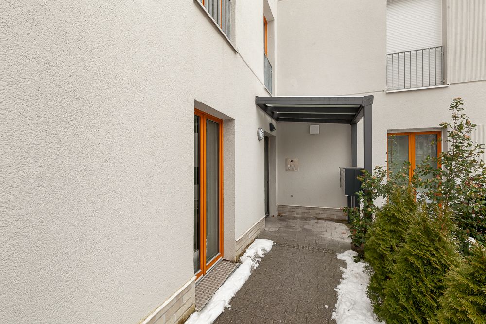 Eingangsbereich eines Wohngebäudes mit Glasdach, Fenstern und etwas Schnee am Boden.