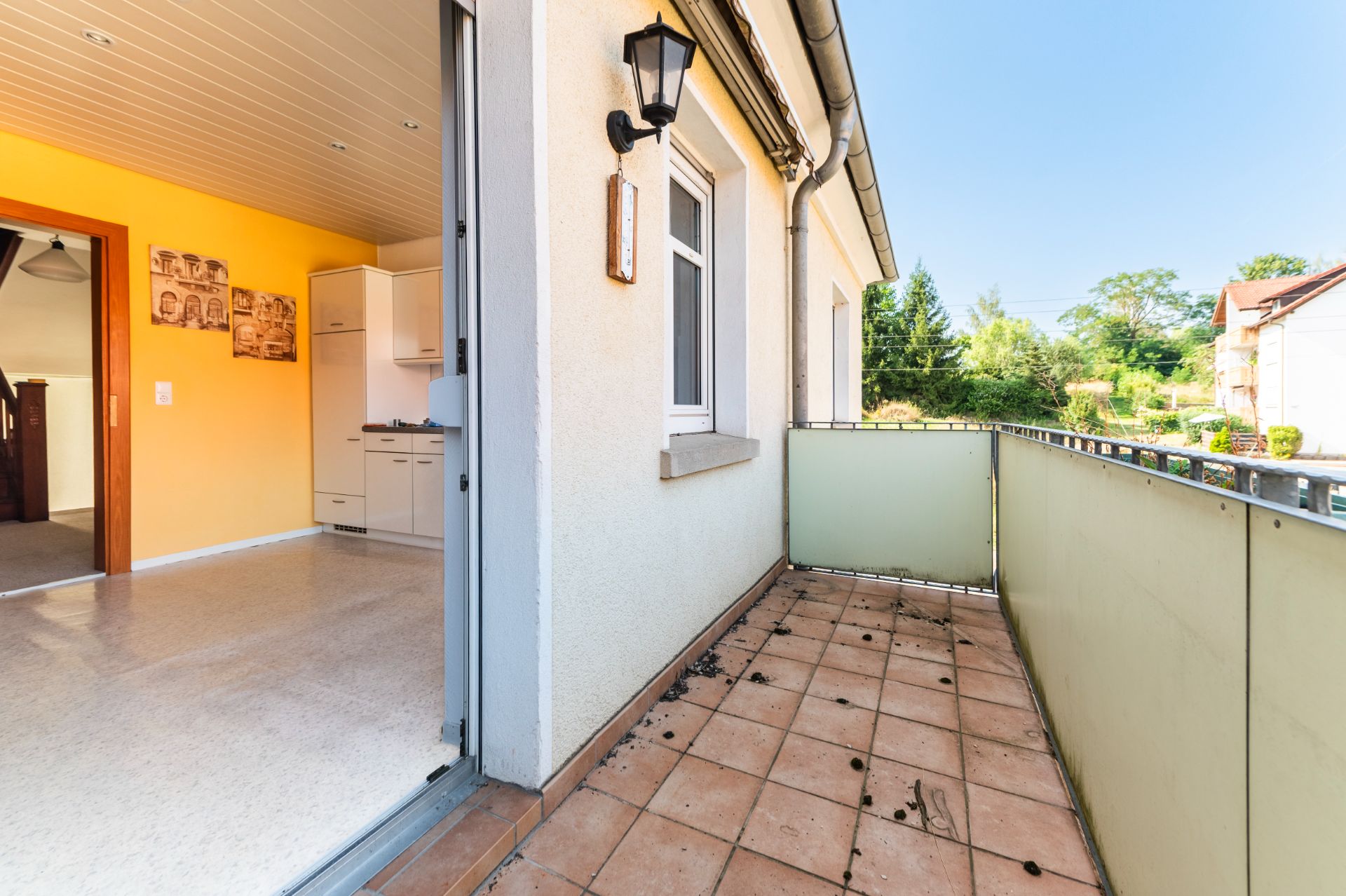 Balkon mit Fliesenboden und Zugang zu einer gelb gestrichenen Küche mit weißen Schränken.