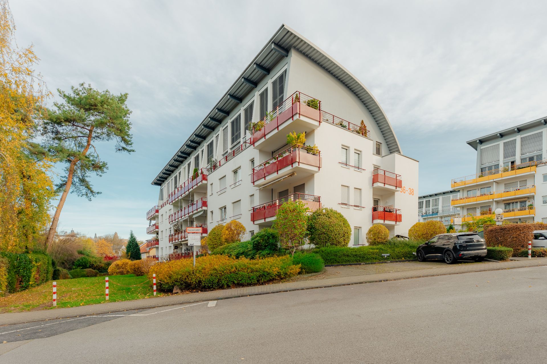 Mehrstöckiges Wohnhaus mit Balkonen, Gartenflächen und parkenden Autos vor dem Gebäude.