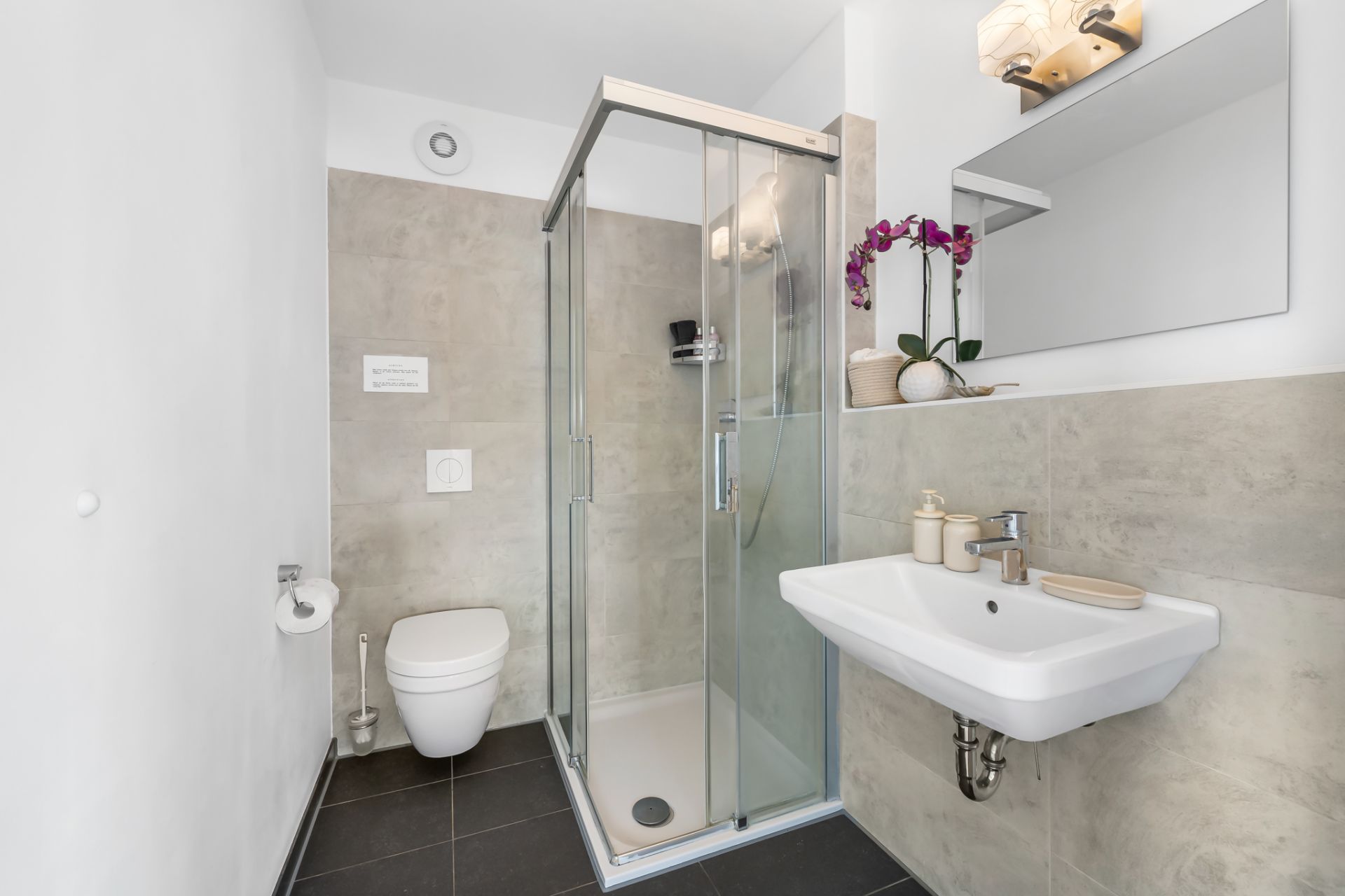 Modernes Badezimmer mit Dusche, WC, Waschbecken, Spiegel und Orchidee auf dem Regal.
