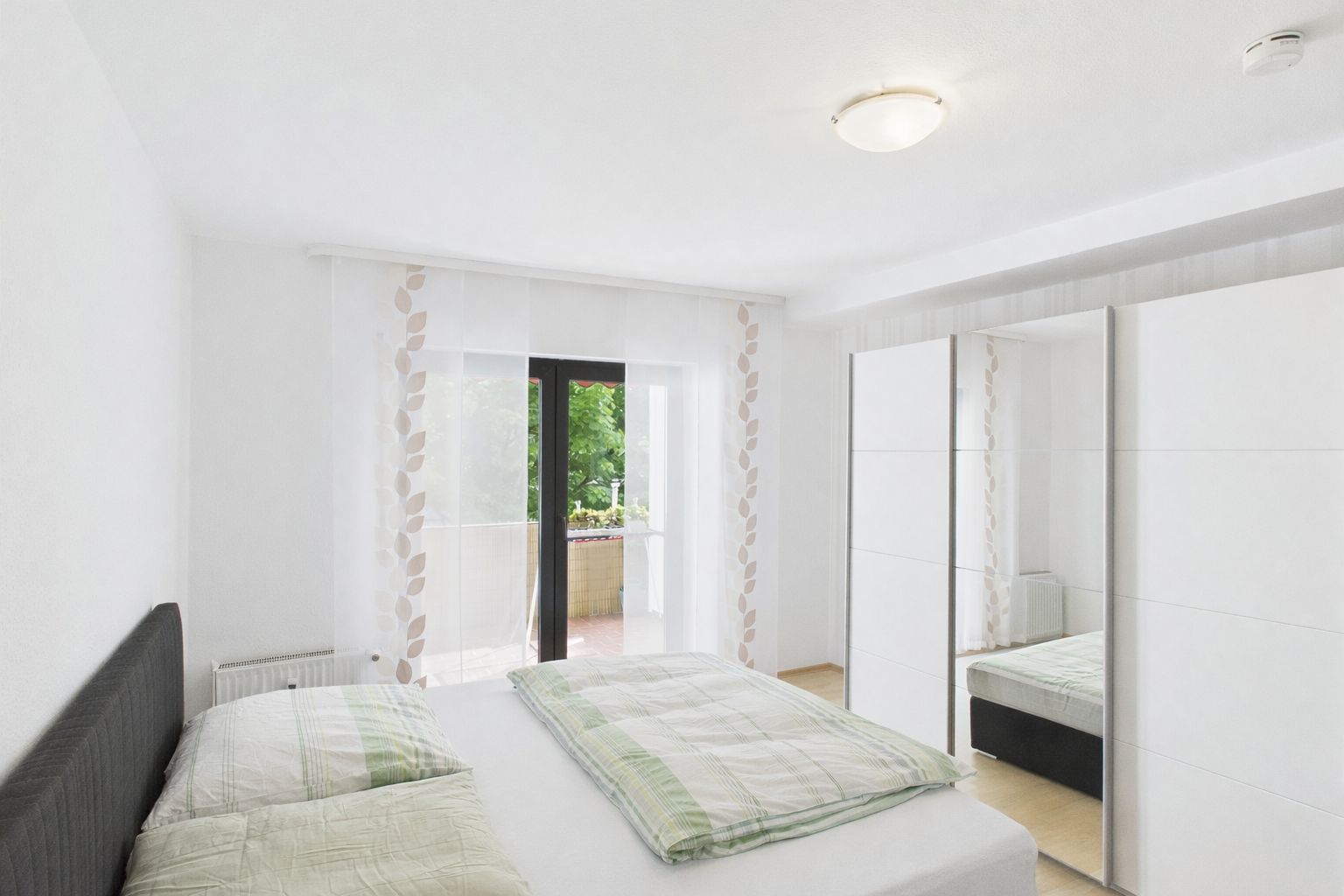 Helles Schlafzimmer mit Doppelbett, großem Kleiderschrank und Zugang zum Balkon.
