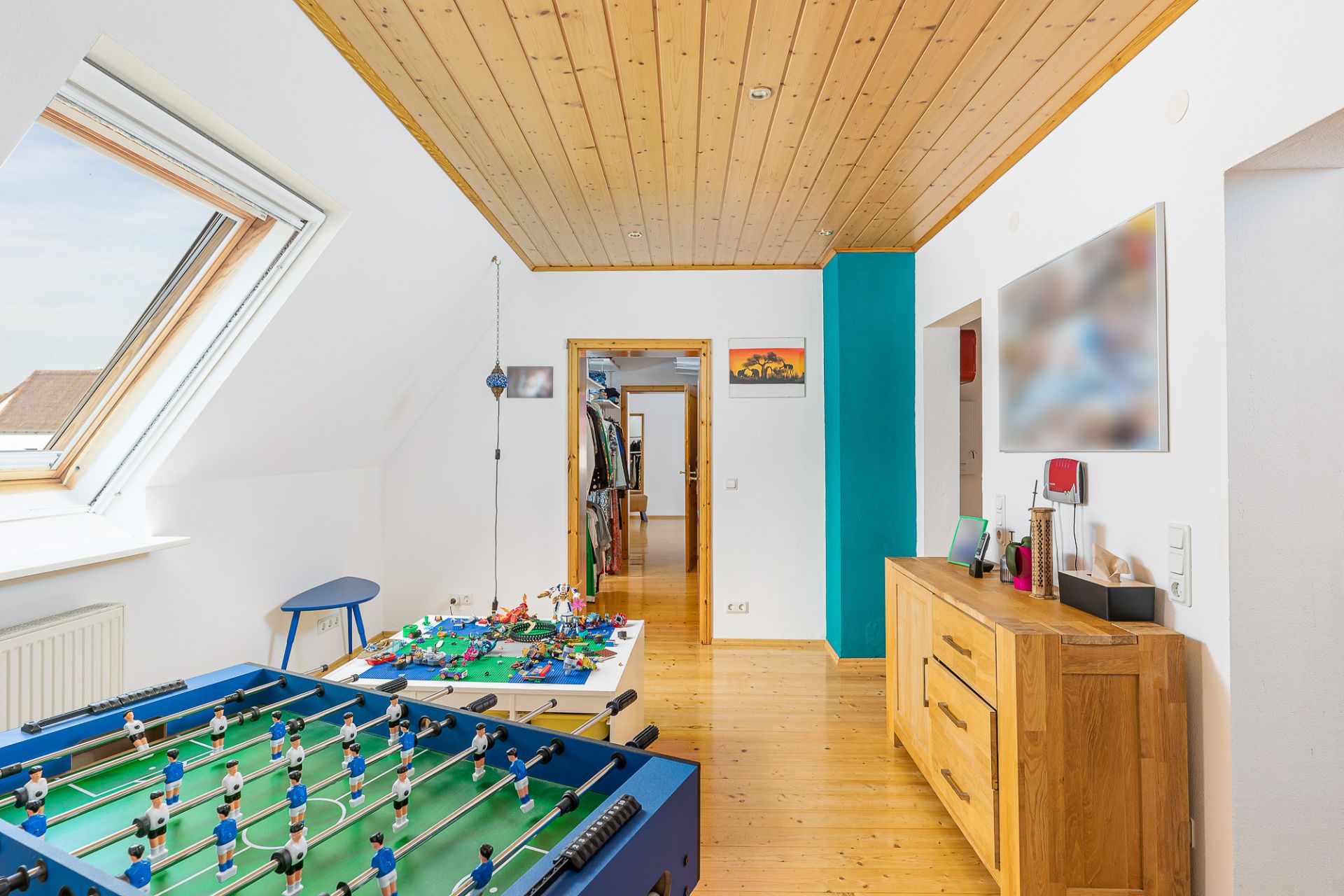 Helles Zimmer mit Holzdecke, Kicker, Spielzeugtisch und Kommode, Dachfenster links.