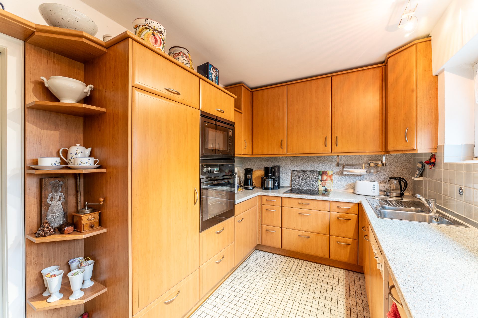 Küche mit Holzschränken, Einbauherd, Spüle und Haushaltsgeräten auf heller Arbeitsfläche.