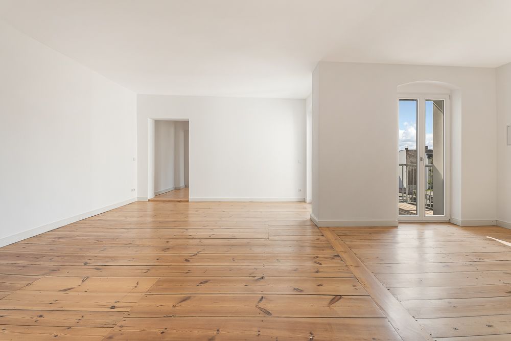Großes, helles Wohnzimmer mit Holzboden und Zugang zu einem Balkon durch eine Glastür.