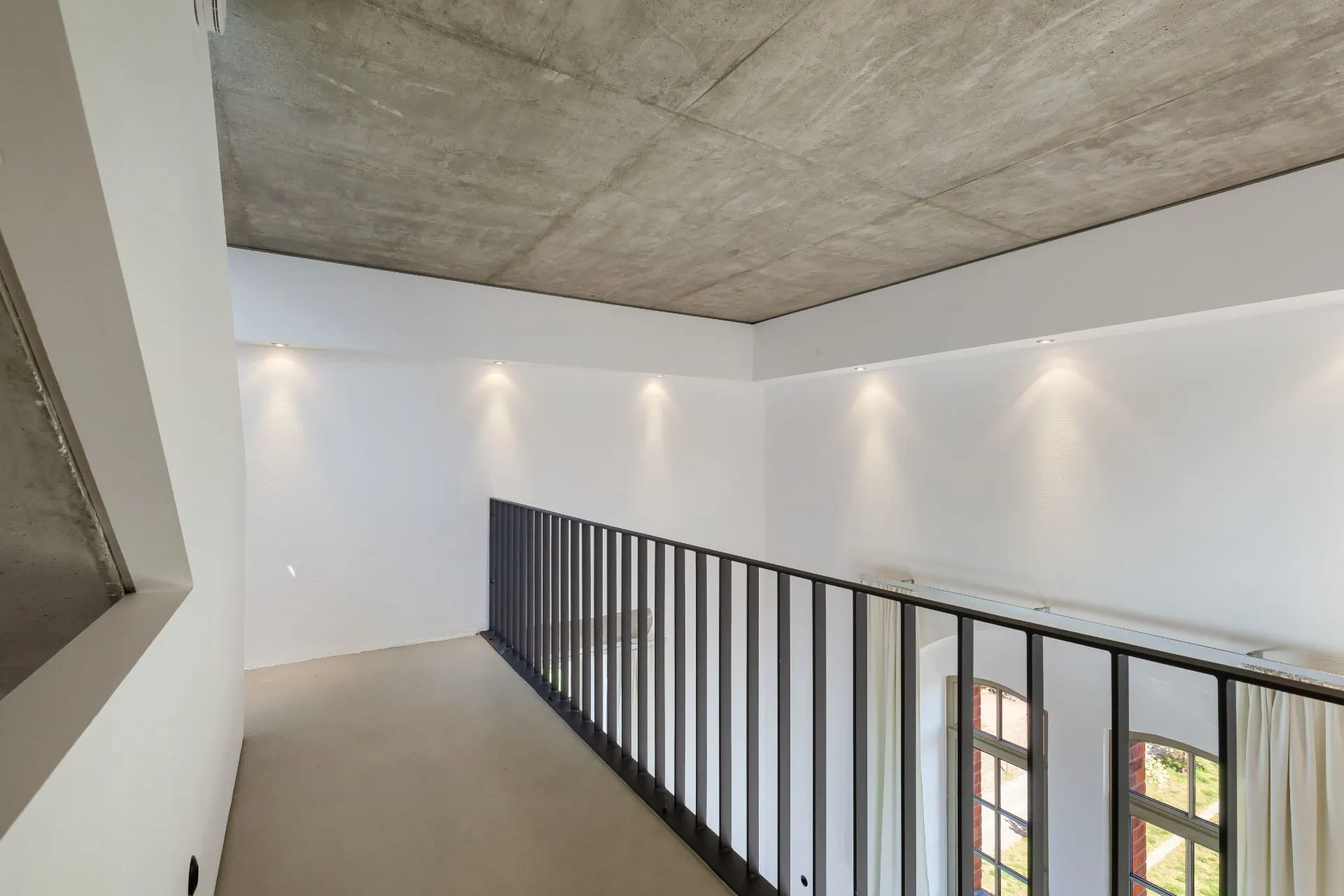 Moderne Galerie mit Metallgeländer, Beton-Decke und weißen Wänden.