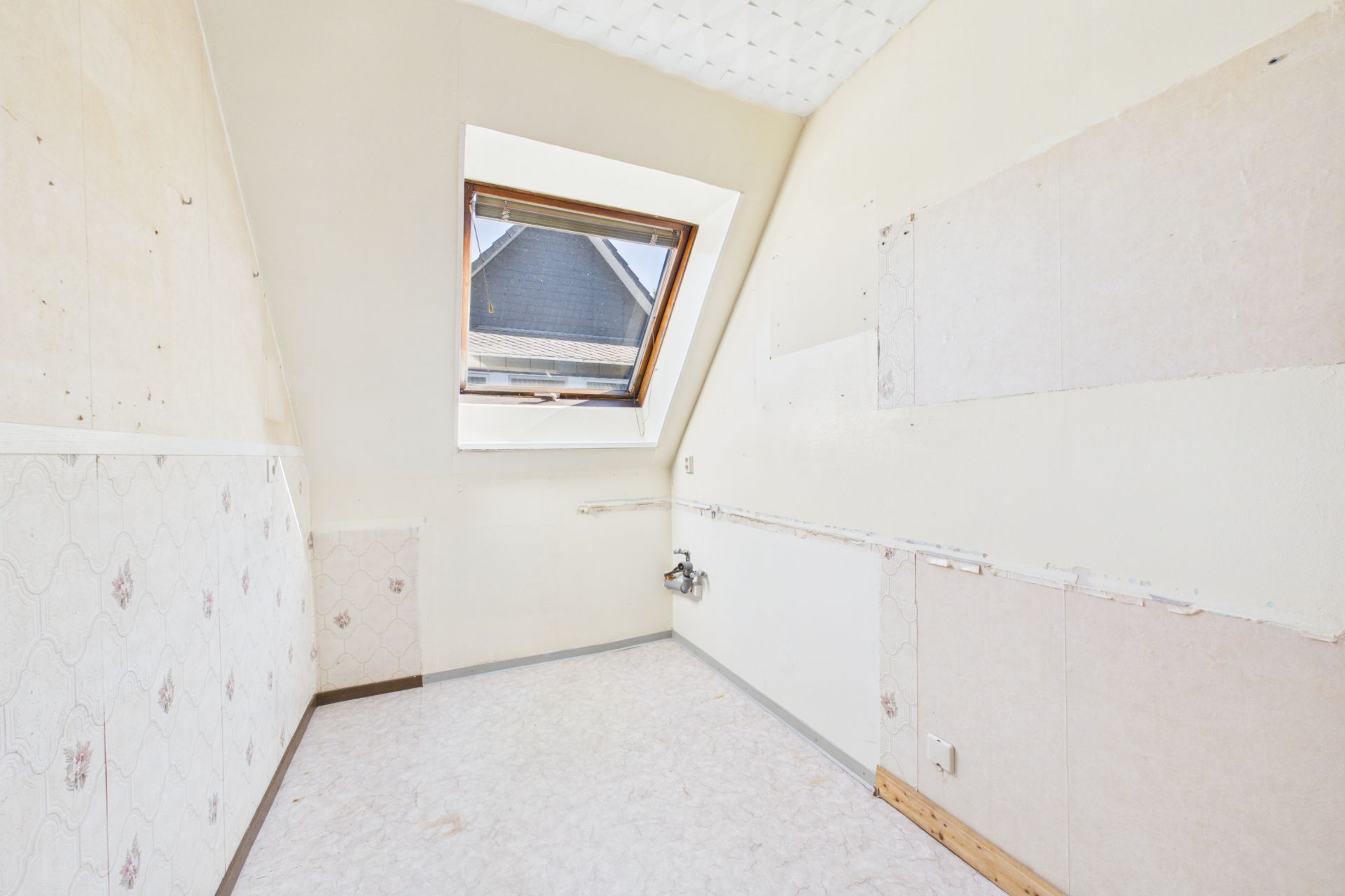 Leerer Raum mit Dachfenster und hellen Wänden, Anschlüsse sichtbar an der Wand.