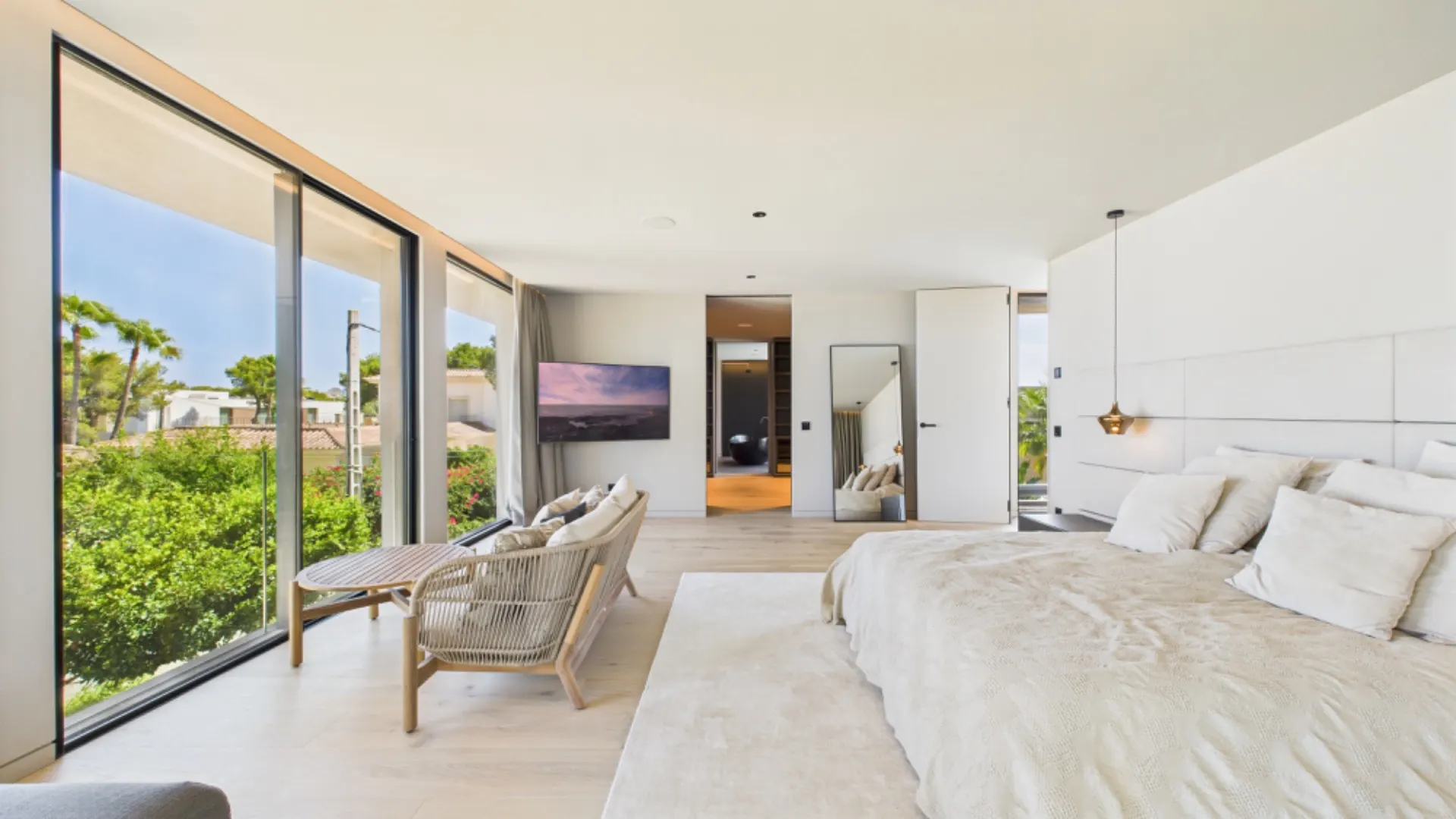 Helles Schlafzimmer mit großem Bett, Sitzbereich und bodentiefen Fenstern mit Gartenblick.