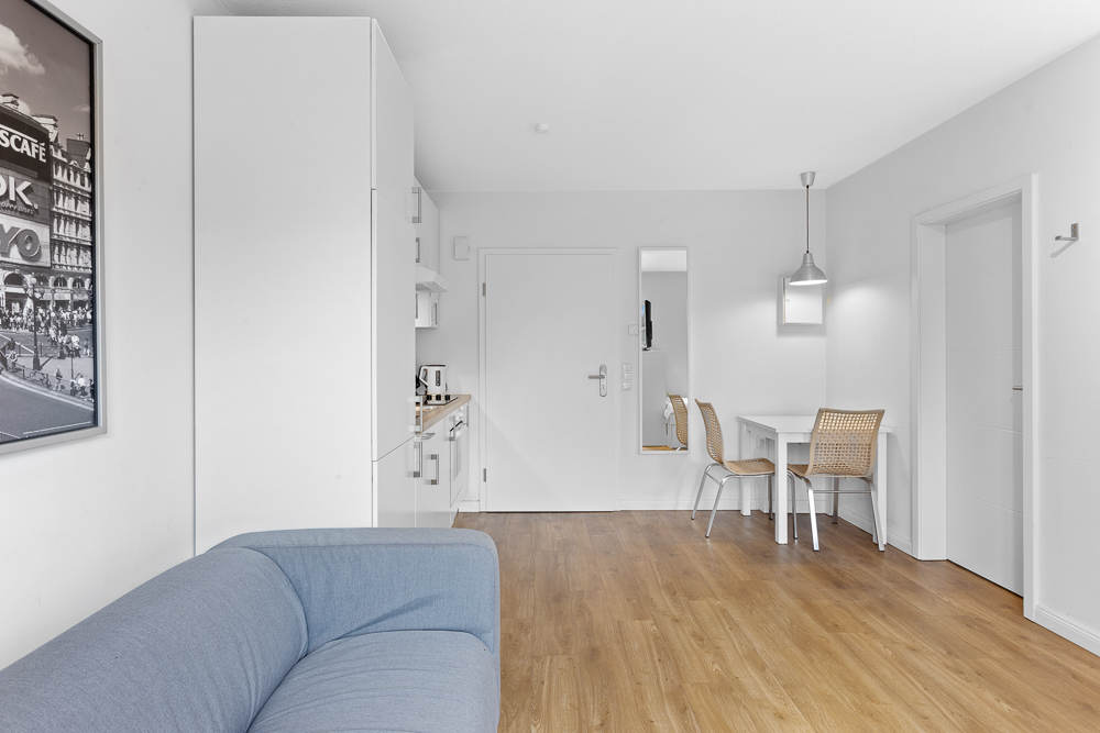 Heller Wohnraum mit blauem Sofa, Holzboden, Esstisch und zwei Stühlen.