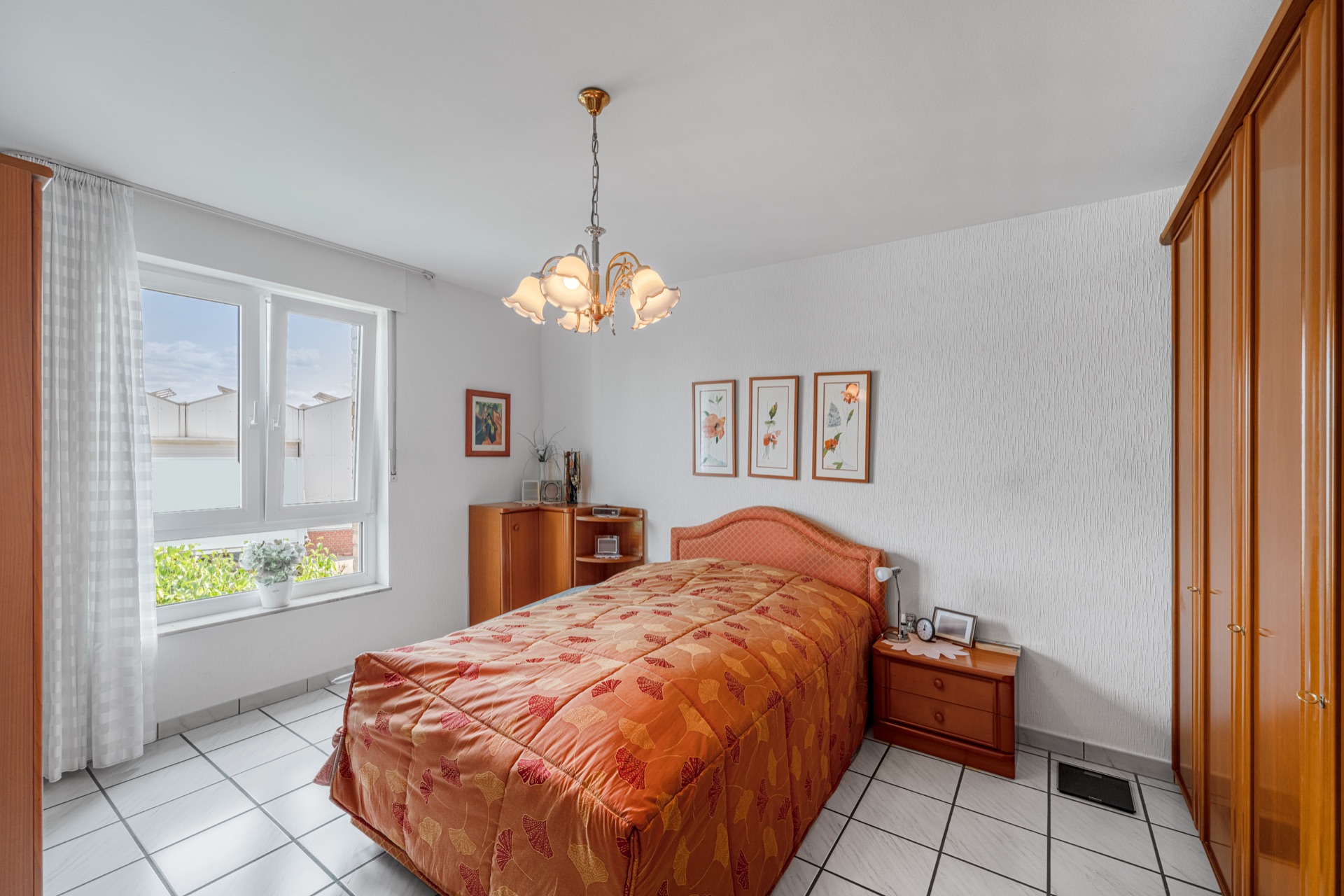 Helles Schlafzimmer mit Doppelbett, Holzschränken und großen Fenstern mit hellen Gardinen.