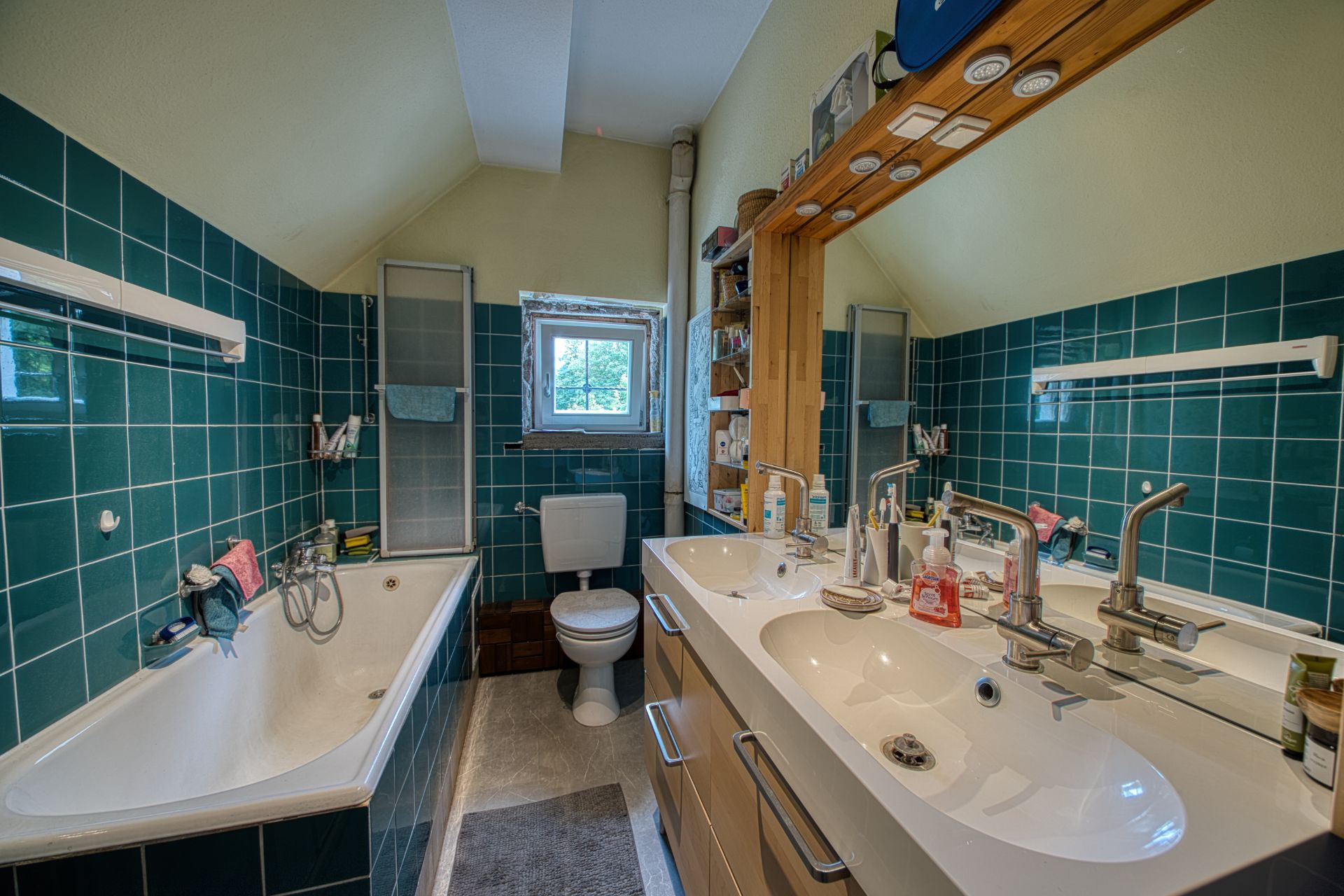 Badezimmer mit Badewanne, Doppelwaschbecken, WC und grün gefliesten Wänden.