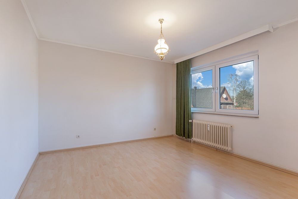 Leeres Zimmer mit Holzfußboden, großem Fenster, Heizung und Deckenlampe.