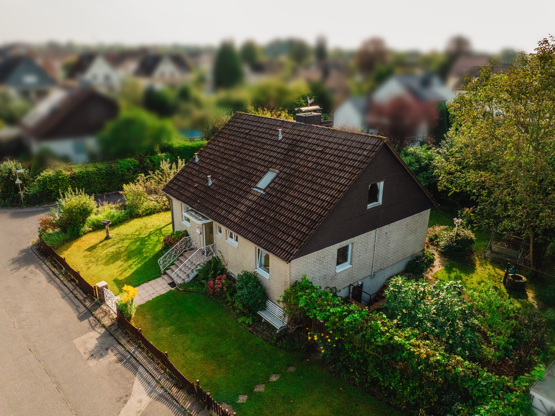 Luftaufnahme eines Einfamilienhauses mit Garten und Vorgarten an einer ruhigen Straße.