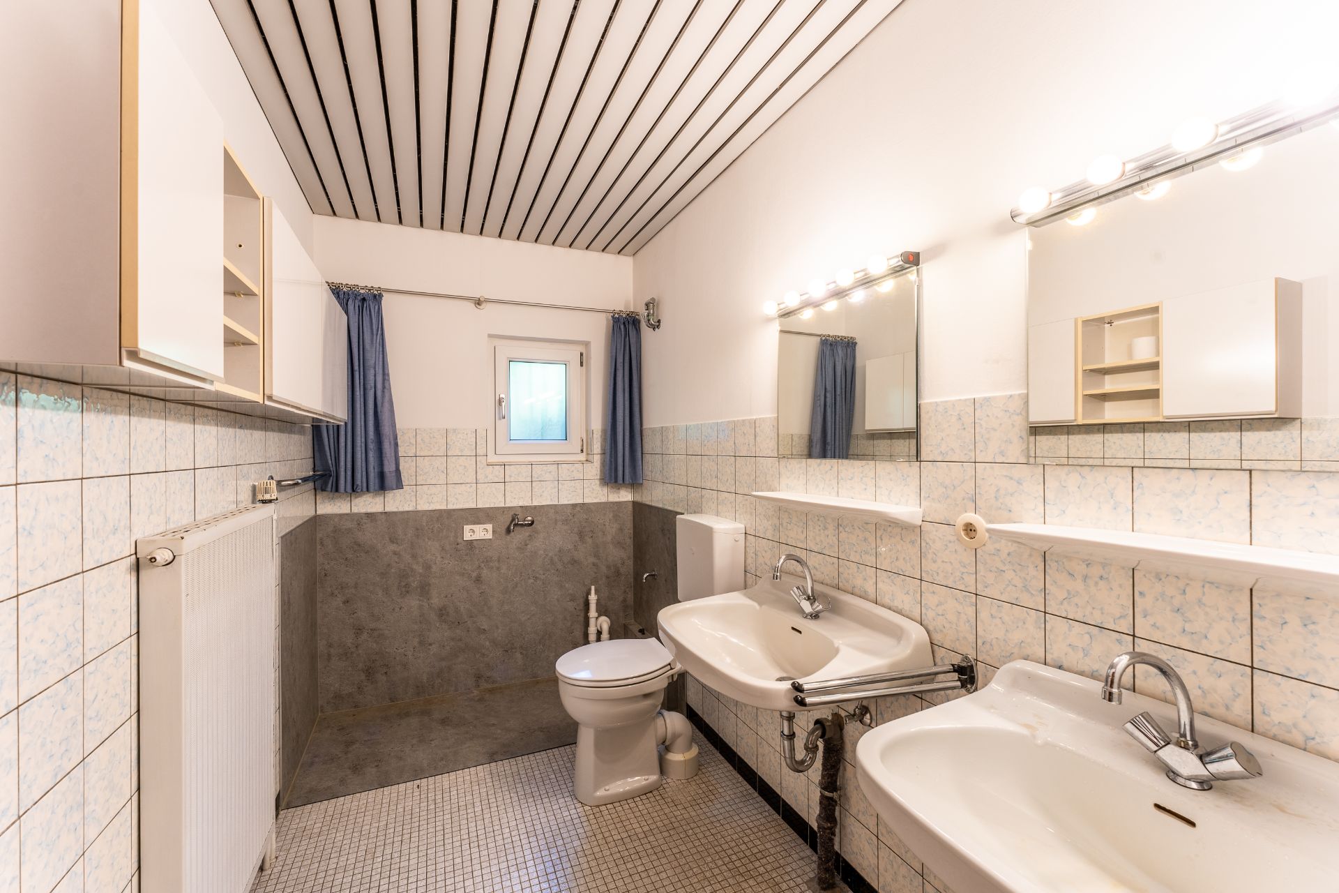 Helles Badezimmer mit zwei Waschbecken, Toilette, Spiegel und weißen Fliesen.
