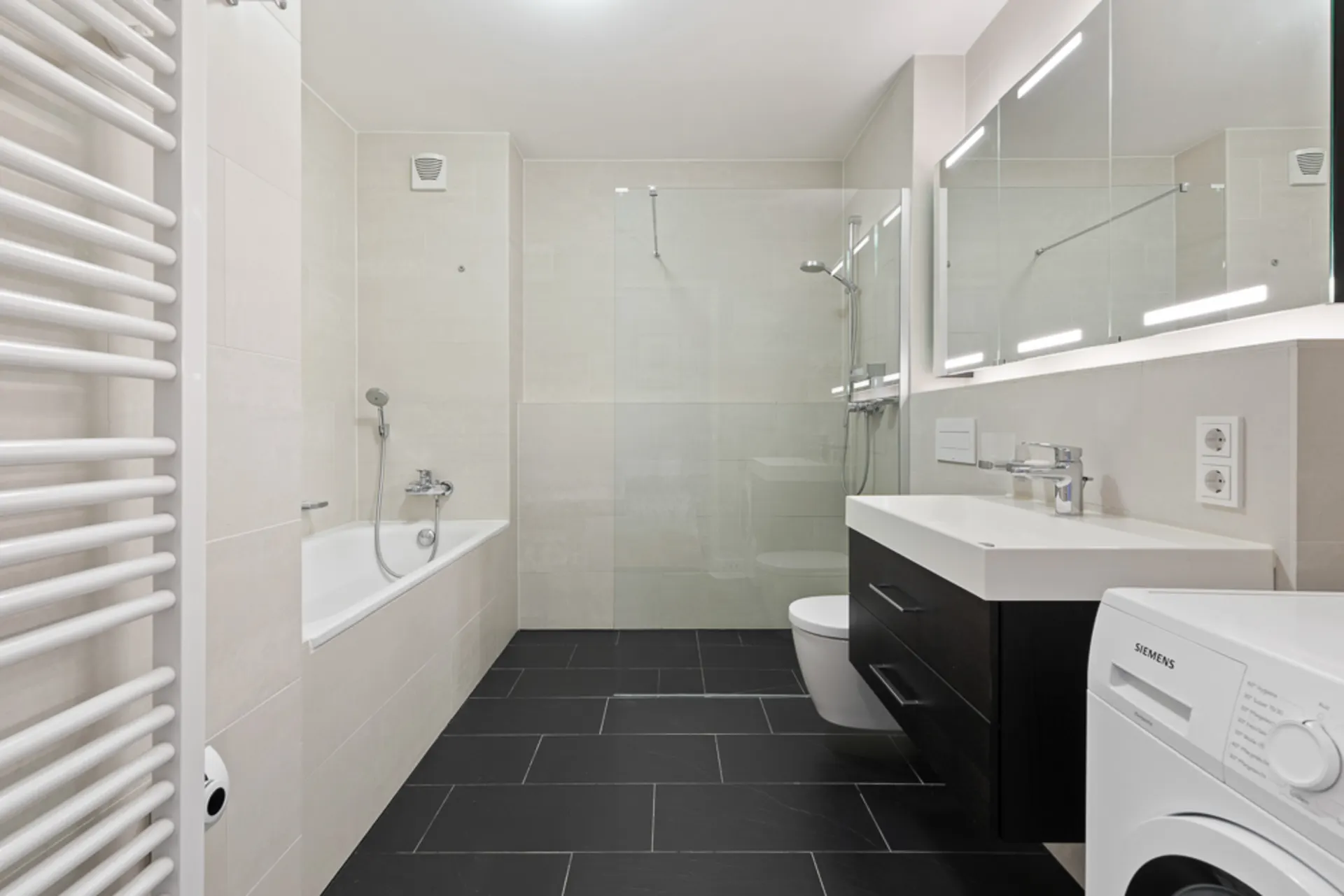 Modernes Badezimmer mit Badewanne, Dusche, Waschbecken, Toilette und Waschmaschine.
