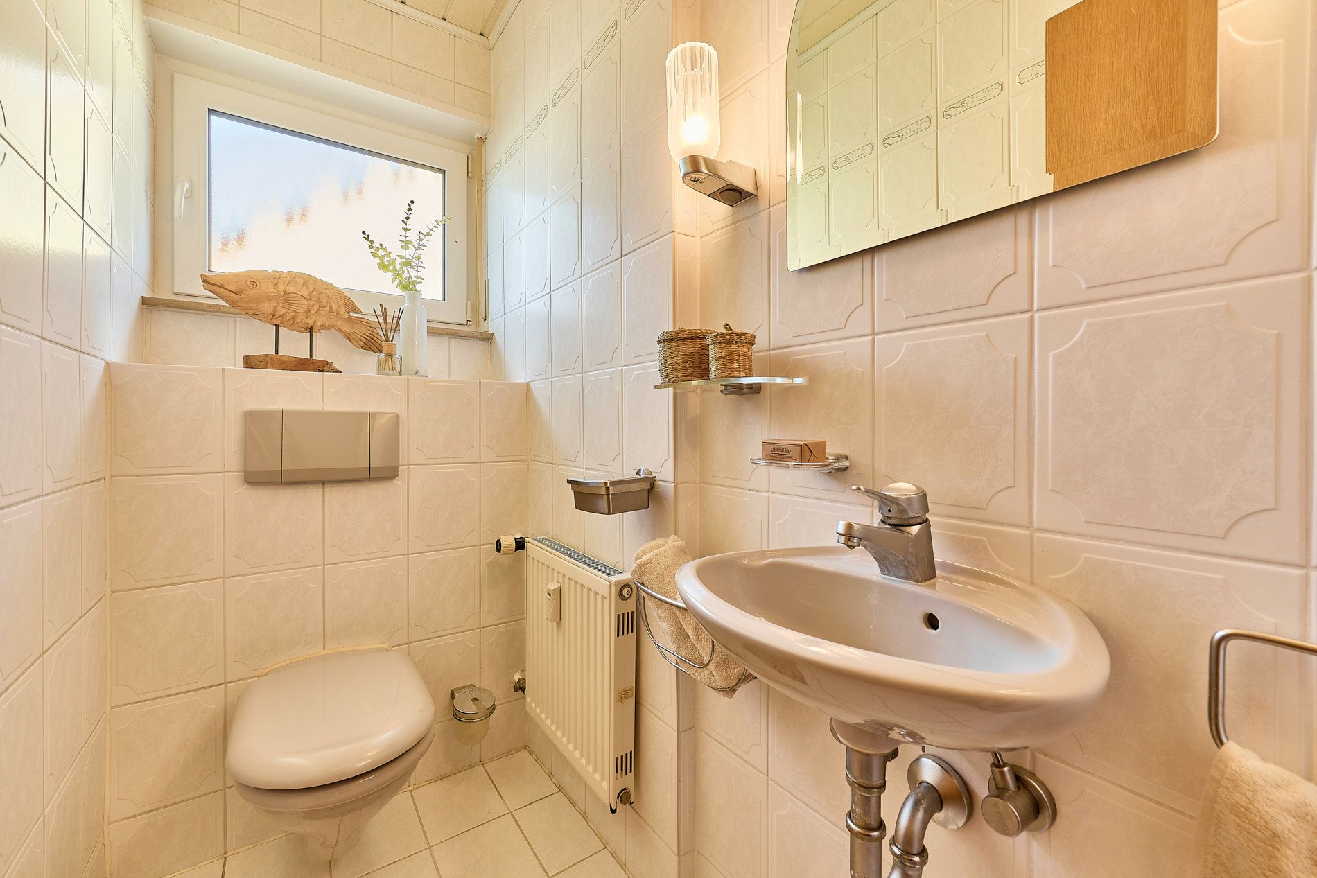 Kleines Badezimmer mit Toilette, Waschbecken, Spiegel und Fenster.