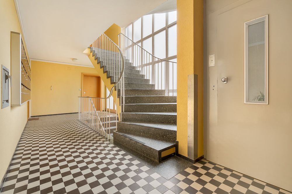 Treppenhaus mit schwarz-weiß kariertem Boden und gelben Wänden in einem Wohngebäude.