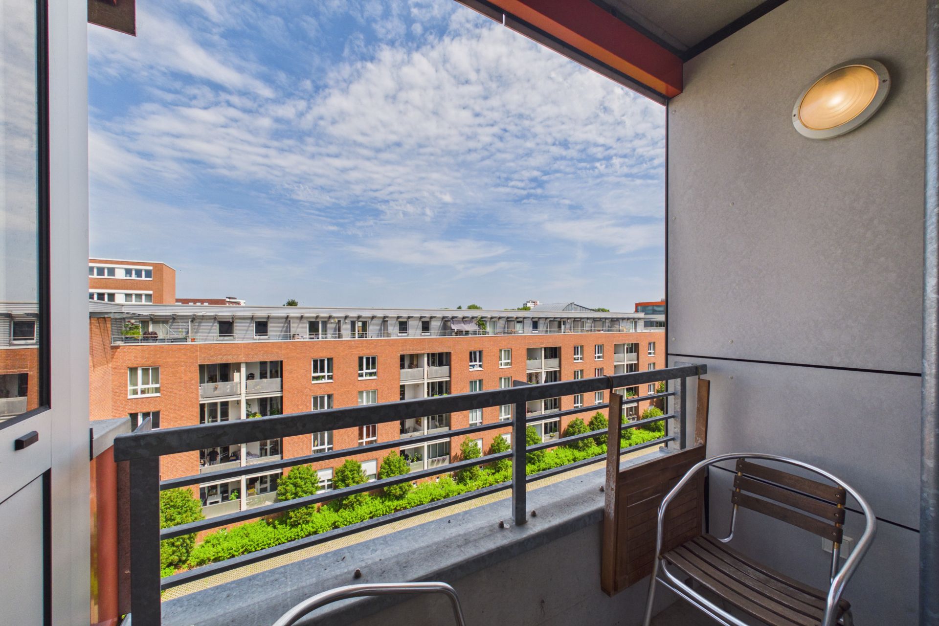 Balkon mit zwei Stühlen und Blick auf ein rotes Wohngebäude und blauen Himmel.