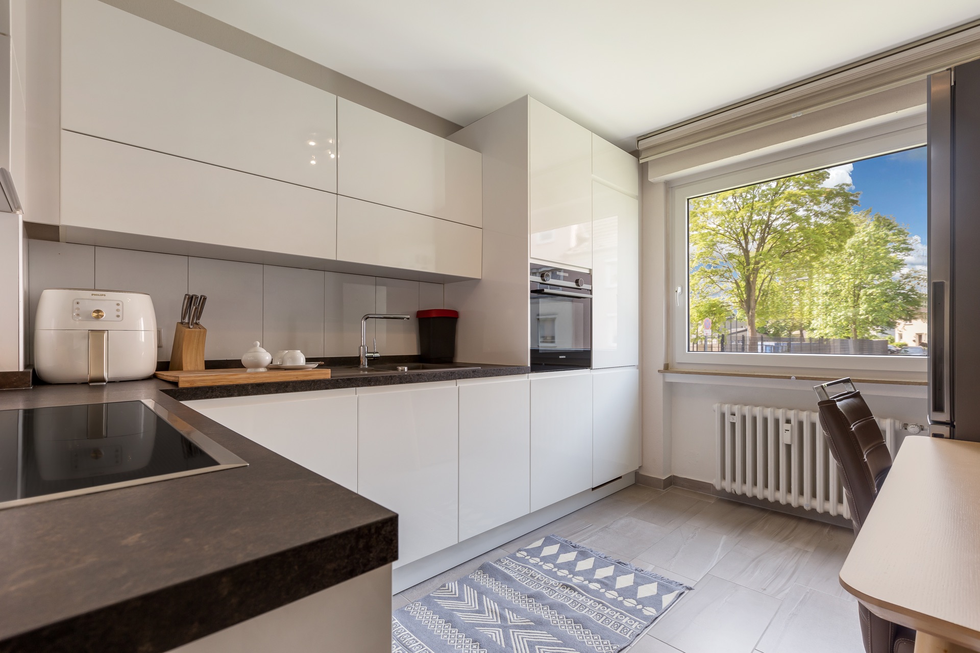Moderne Küche mit weißen Schränken, großem Fenster und Küchenutensilien auf der Arbeitsfläche.