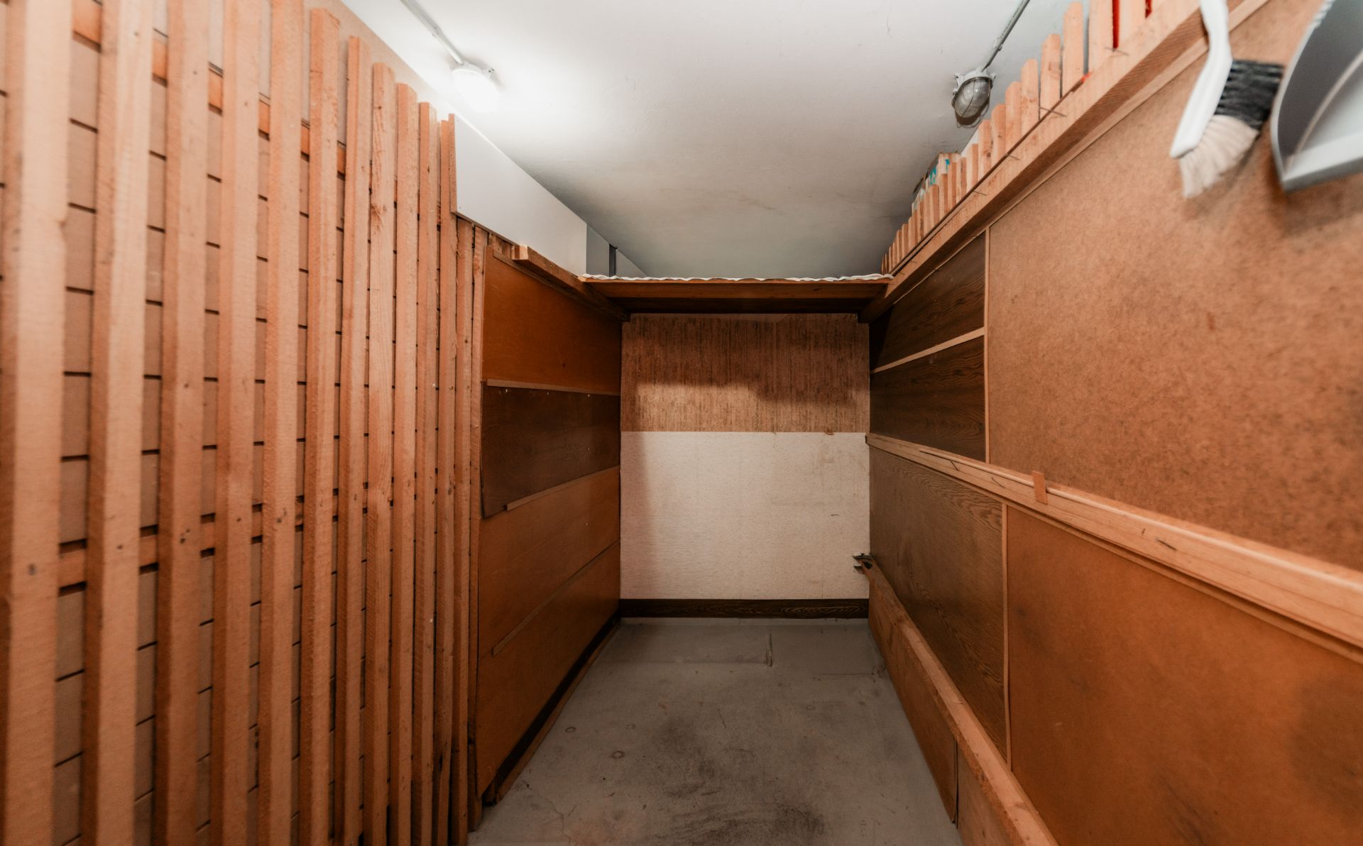 Schmaler Abstellraum mit Holzwänden und Regalen unter einer weißen Decke.