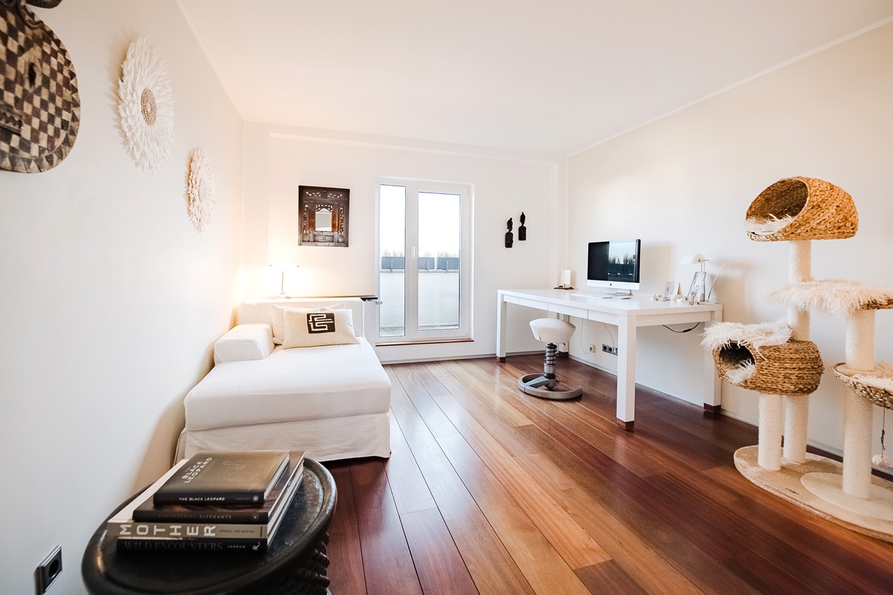 Helles Zimmer mit Holzboden, Sofa, Schreibtisch mit Computer und Kratzbaum.