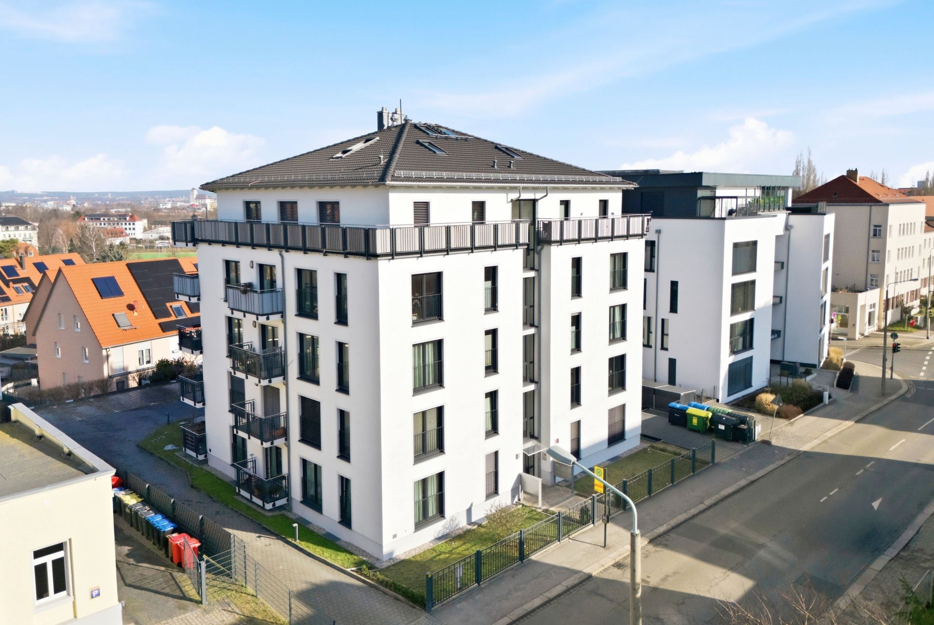 Modernes, mehrstöckiges Wohnhaus mit Balkonen an einer Straßenecke bei Tageslicht.