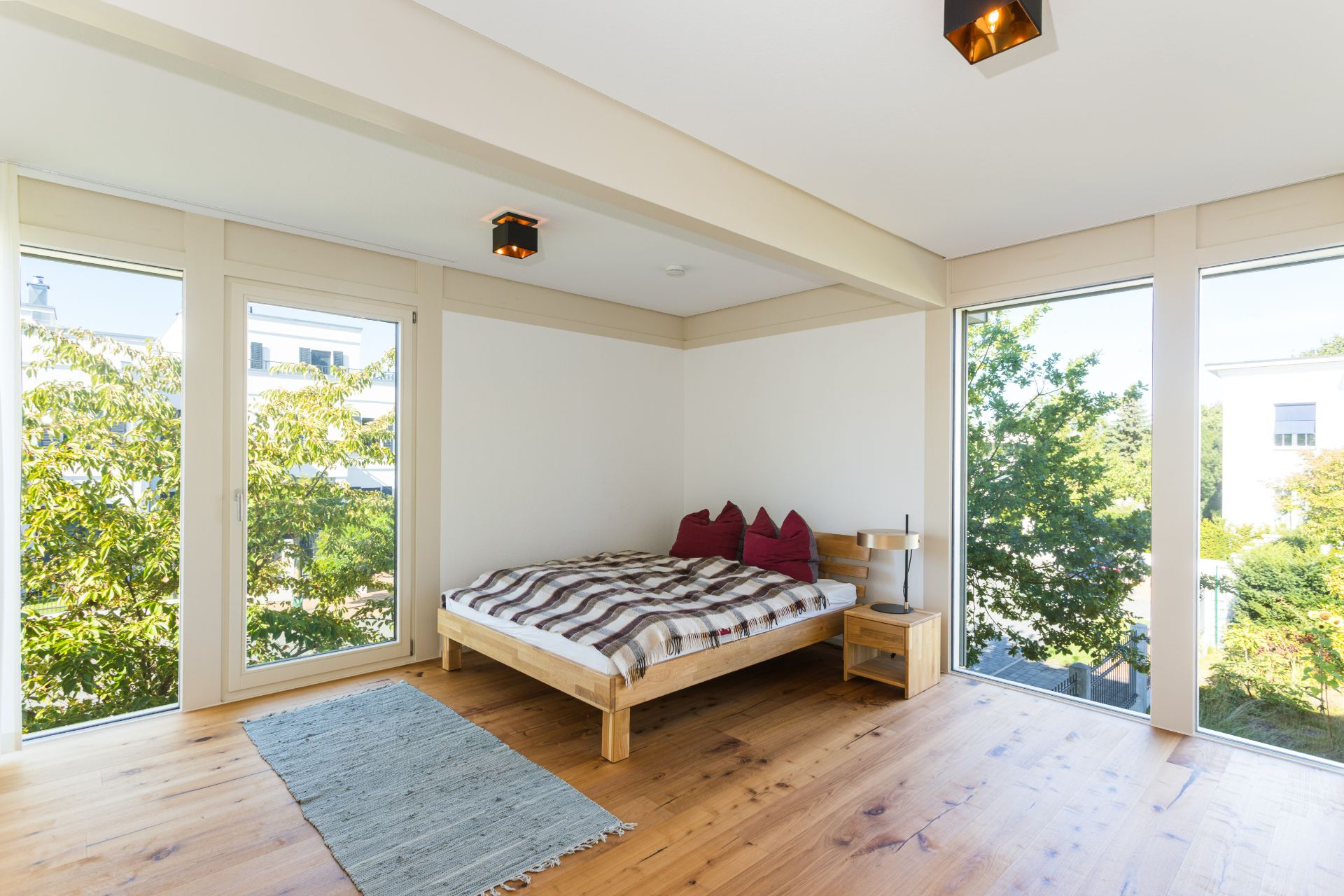 Helles Schlafzimmer mit großem Bett, Holzboden, Teppich und großen Fenstern mit Blick ins Grüne.