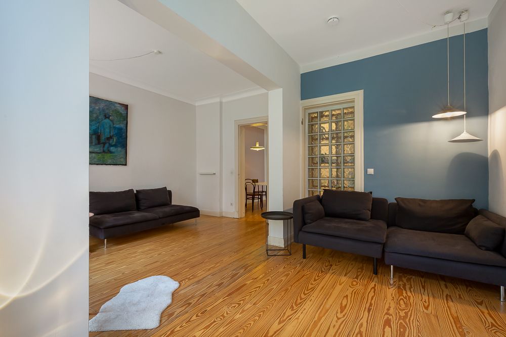 Wohnzimmer mit Holzboden, zwei dunklen Sofas, kleinem Tisch und blauer Akzentwand.