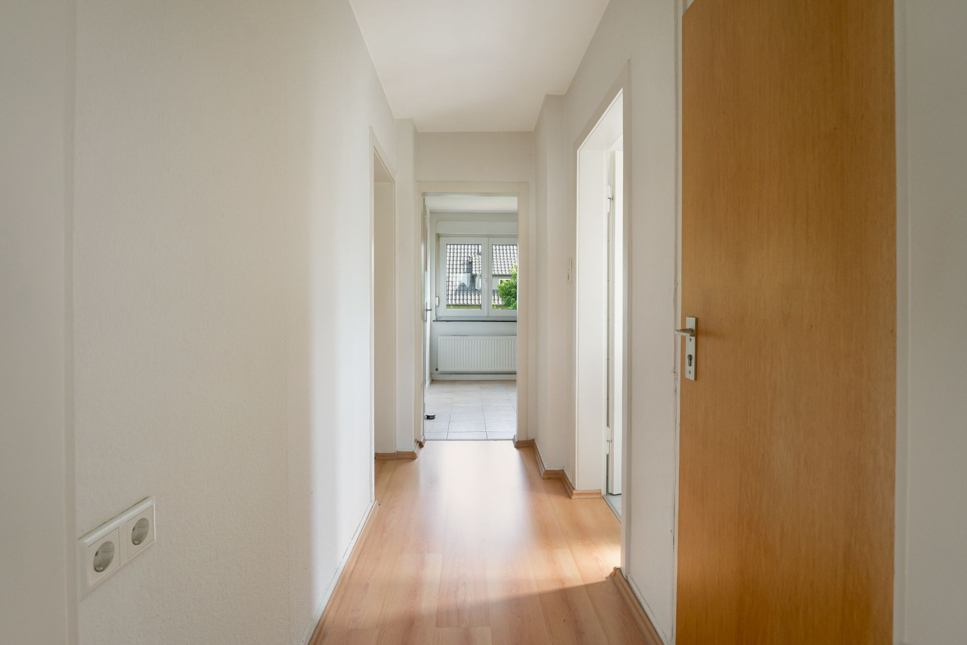 Heller Flur mit Holzfußboden, mehreren Türen und Blick in einen Raum mit Fenster.