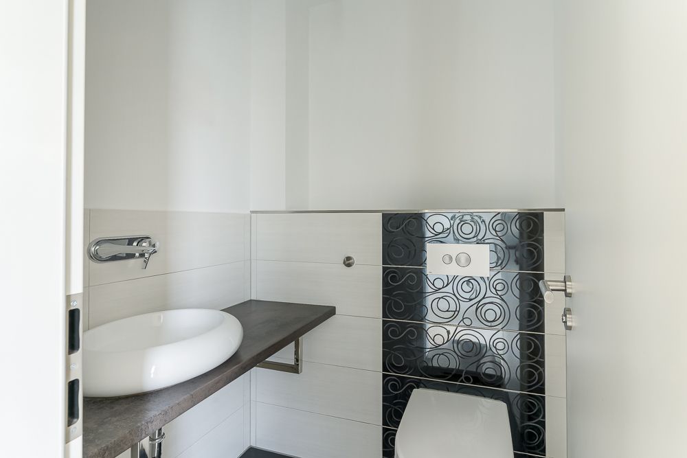 Modernes kleines Bad mit rundem Waschbecken, Wandarmatur und WC mit schwarzer Fliesenverzierung.