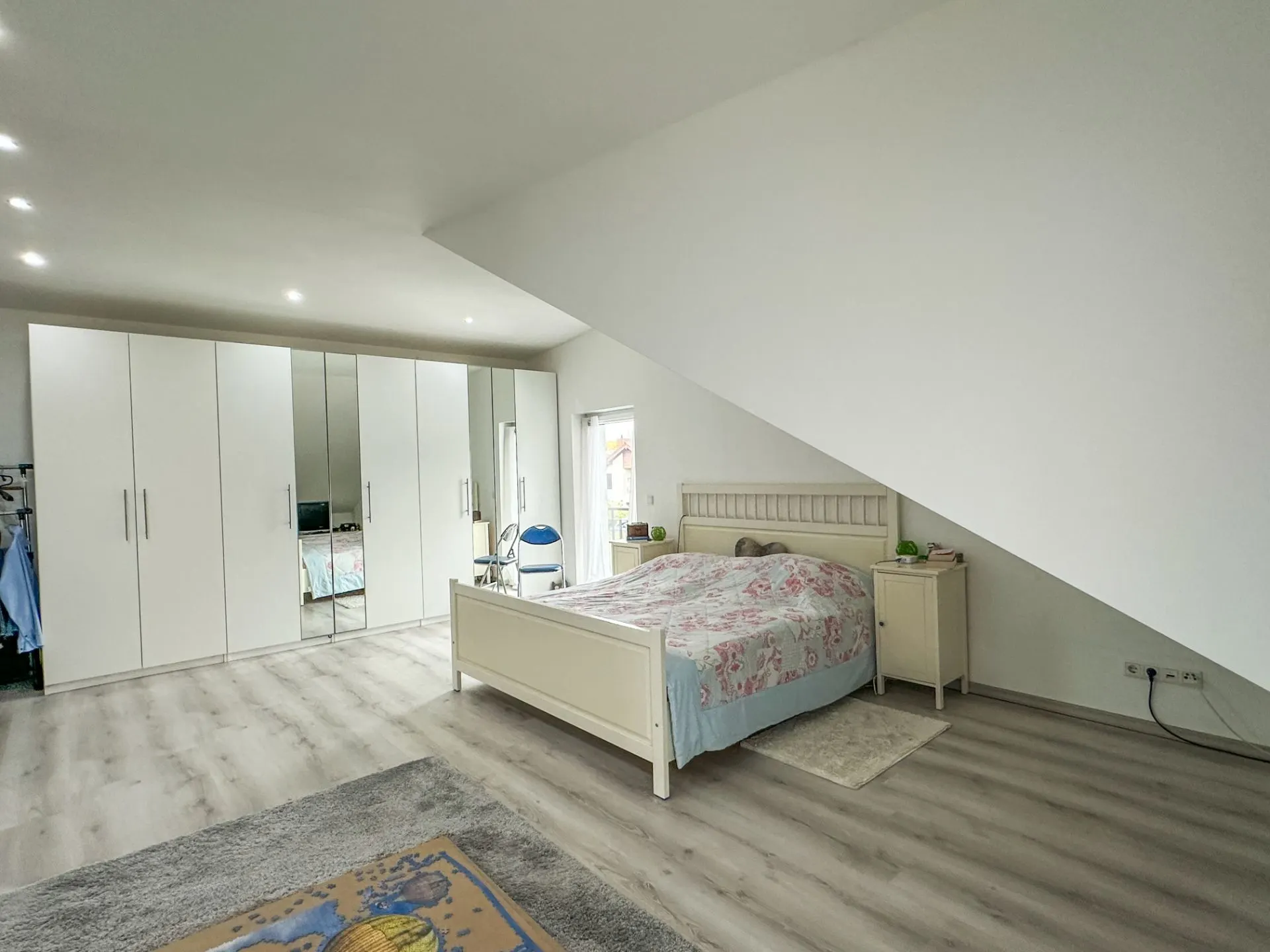 Helles Schlafzimmer mit großem weißen Kleiderschrank, Bett und Nachttisch unter einer Dachschräge.
