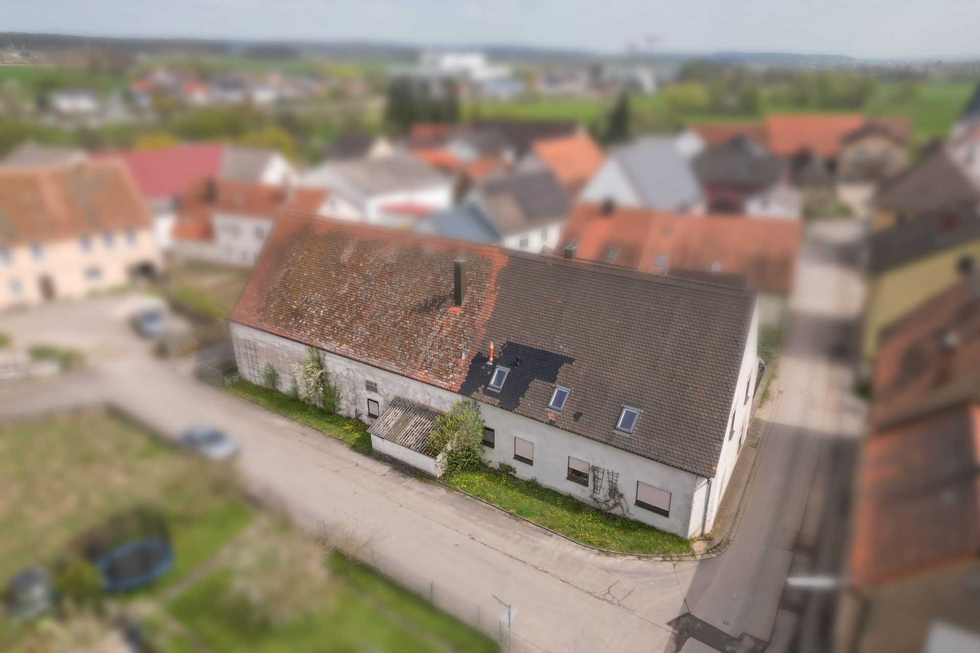 Wohnhaus mit Schrägdach an einer Straßenecke, umgeben von weiteren Häusern.