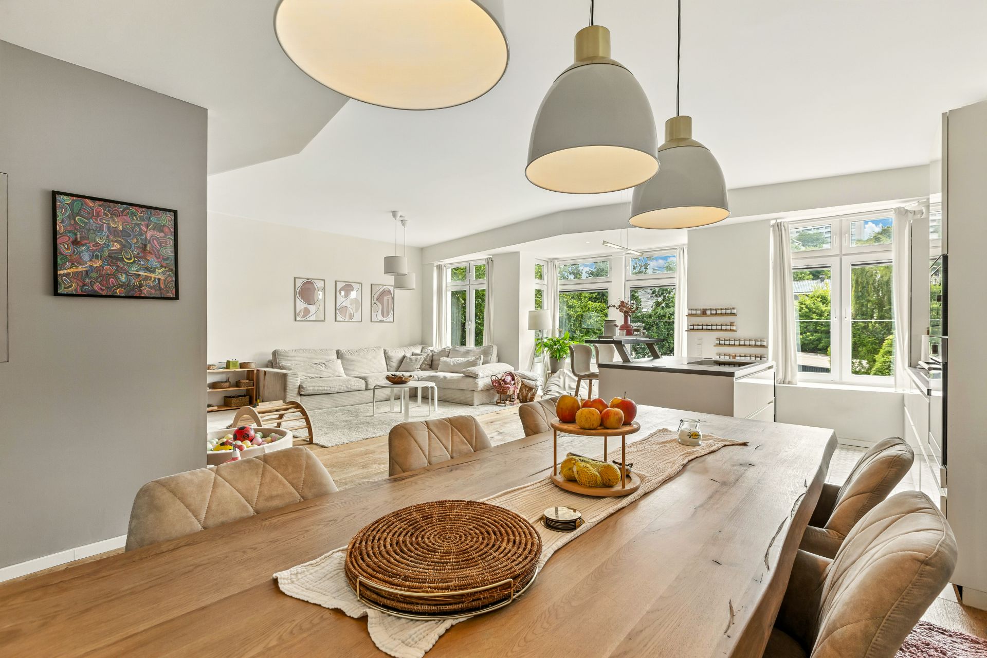 Helles Wohnzimmer mit Esstisch, bequemen Stühlen, Sofa und großen Fenstern mit Blick ins Grüne.